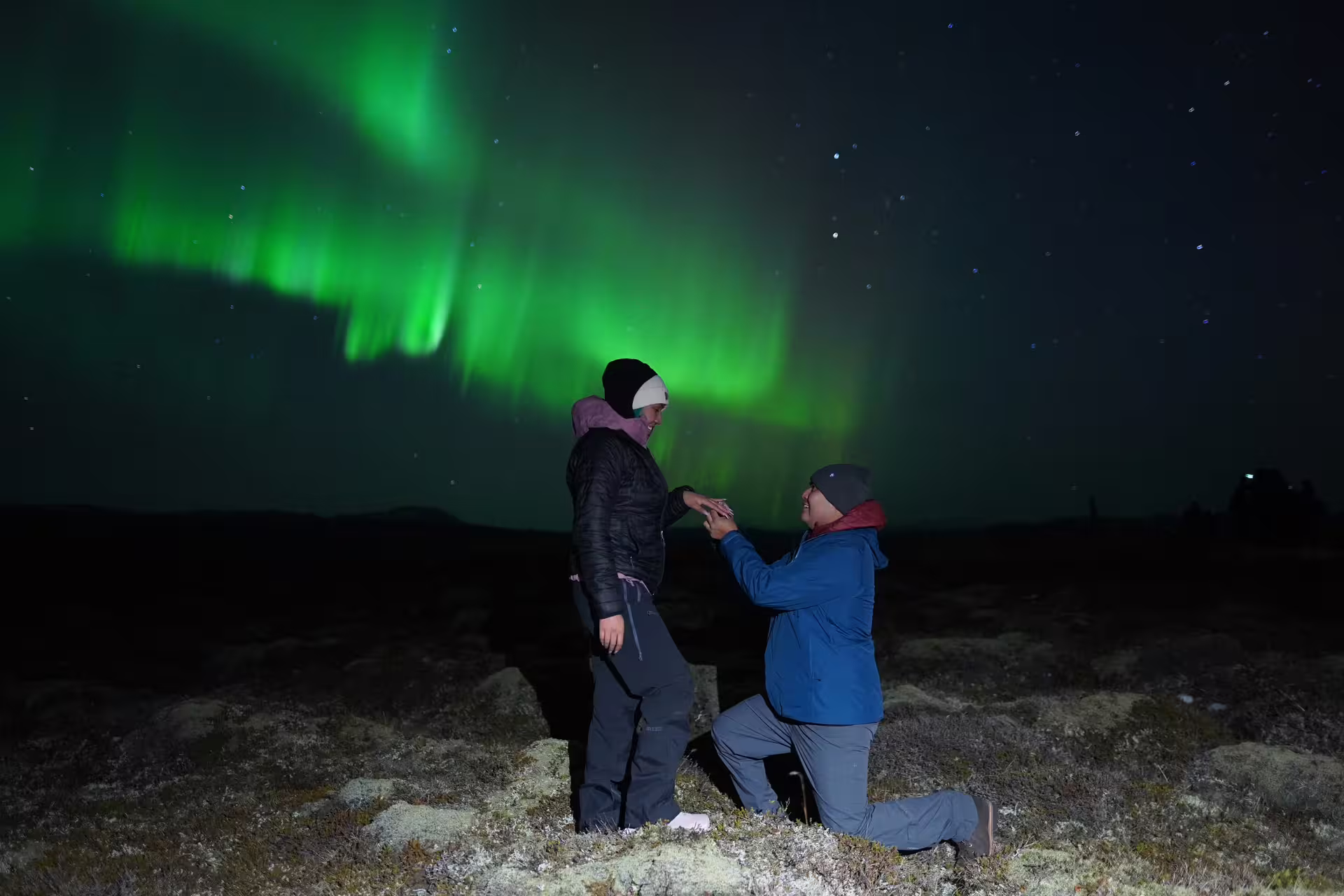 Couple proposal under vibrant green northern lights aurora borealis in Iceland night sky