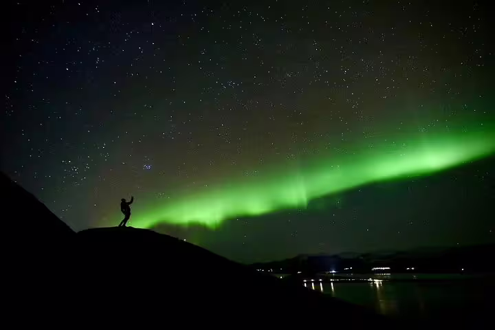 Silhouette of person standing on hill beneath vibrant green northern lights over Iceland's night sky