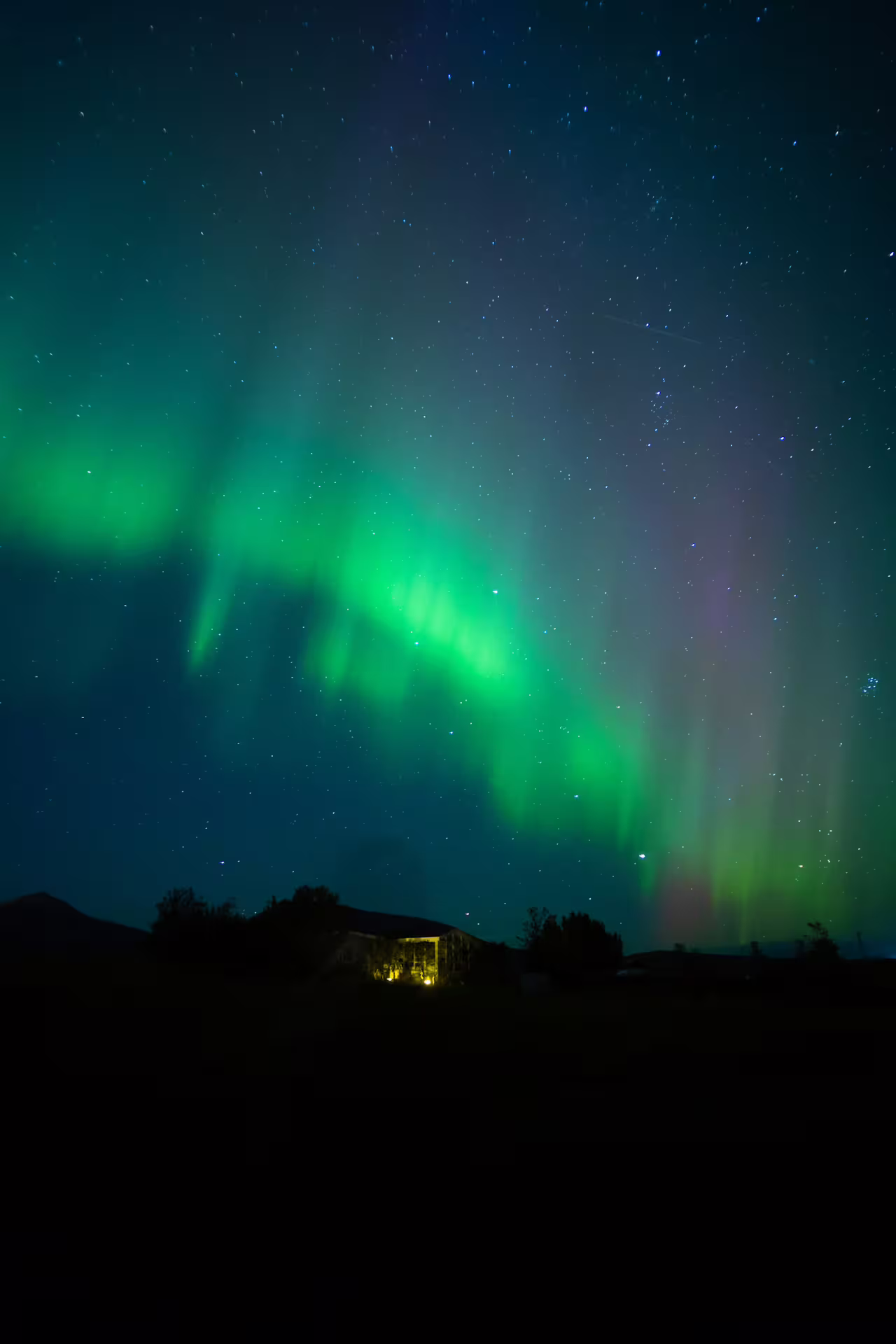 Vivid green northern lights aurora borealis over a small illuminated building in Iceland at night
