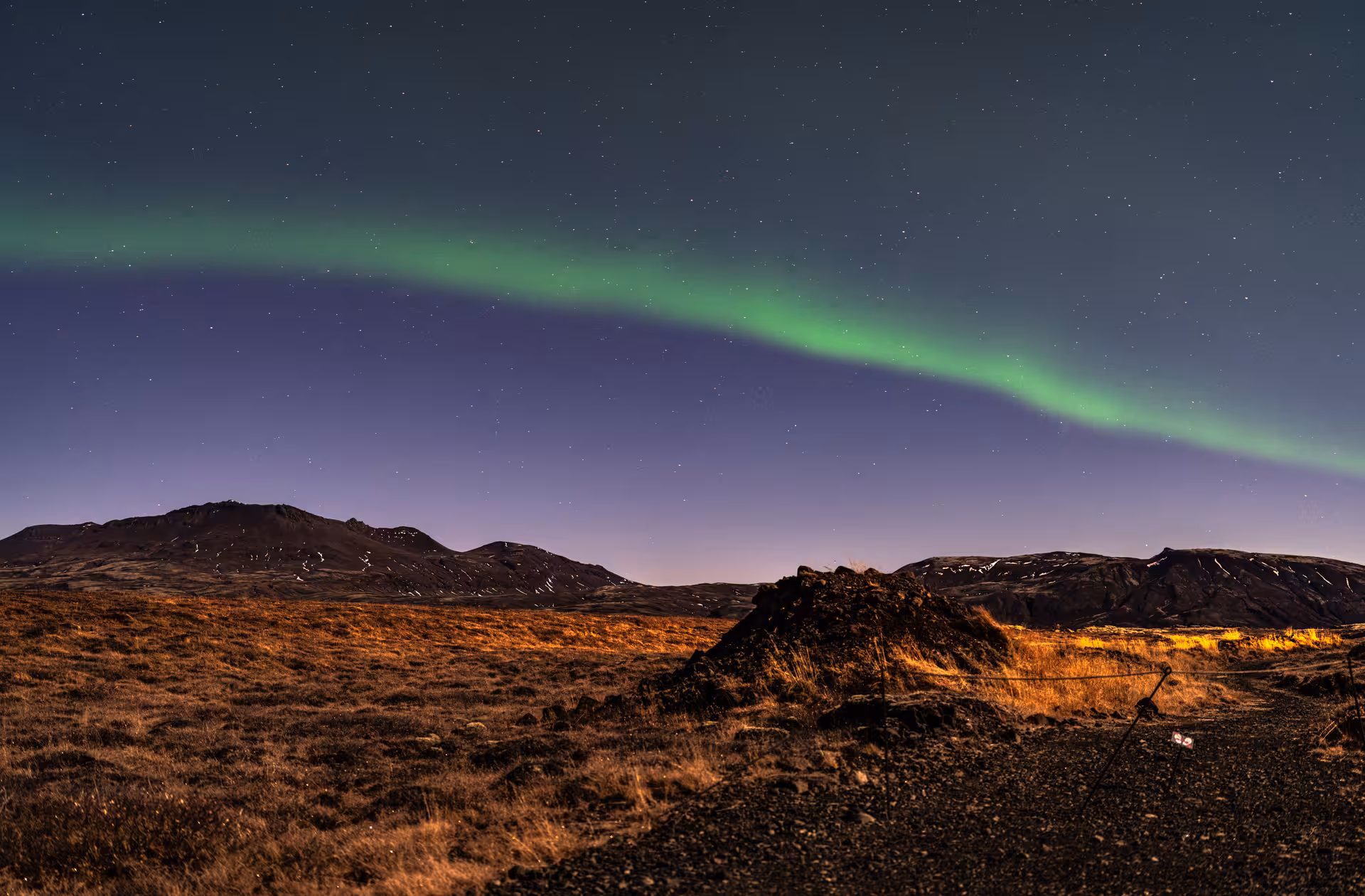 Green northern lights arching over Iceland's volcanic highland landscape under a starry night sky