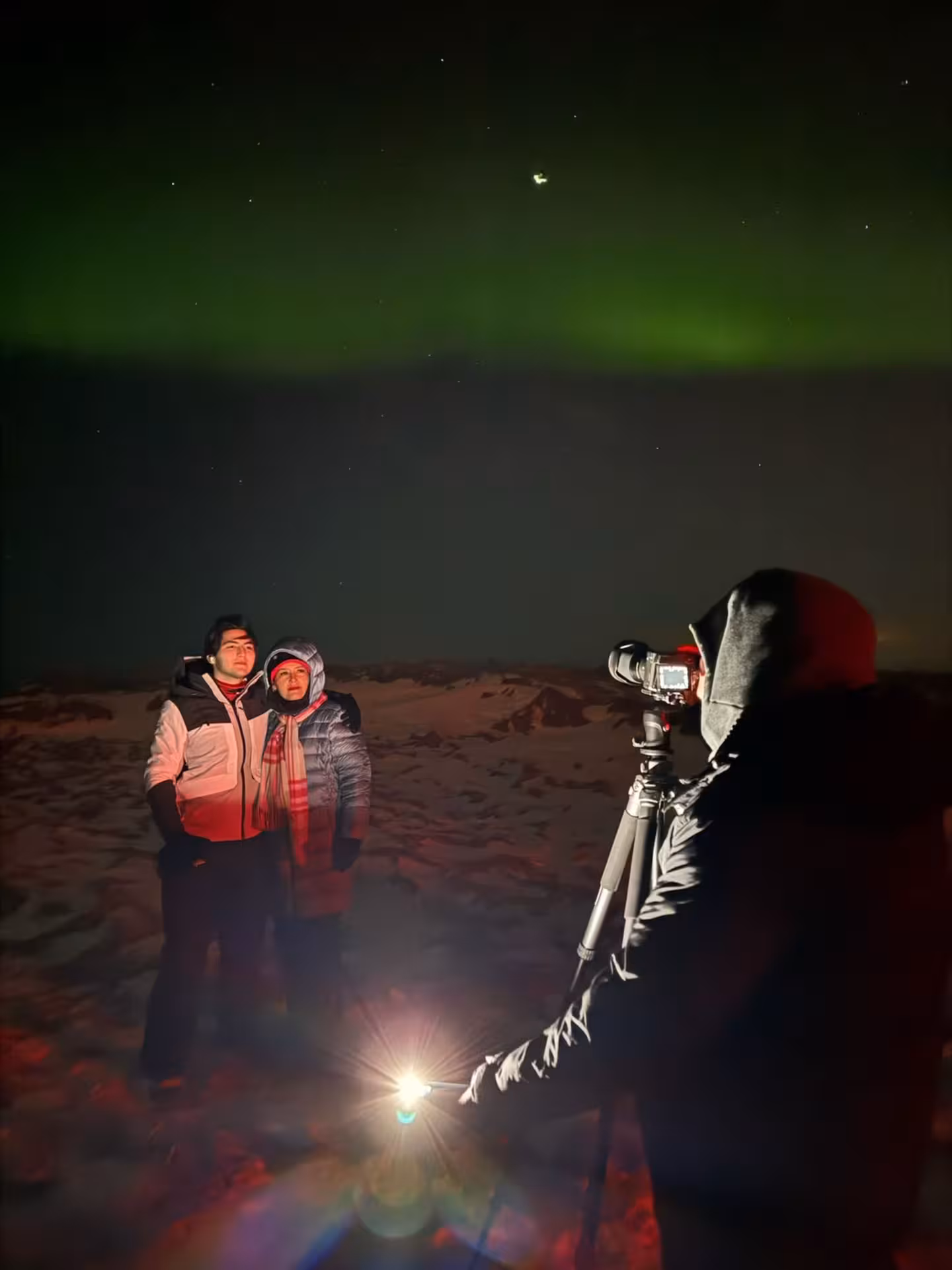 Tour guide photographing guests with a tripod under glowing green northern lights on a private 4x4 aurora hunt in Iceland