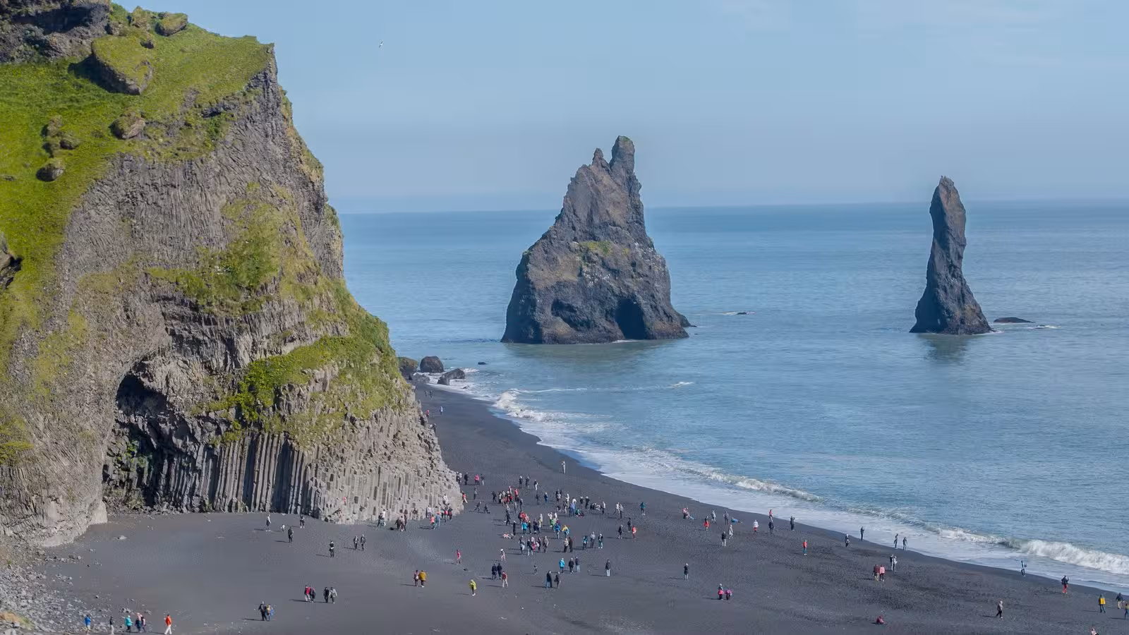 Visitors explore the iconic Reynisfjara black sand beach and sea stacks on Iceland's 12-Day Self-Drive Grand Tour.
