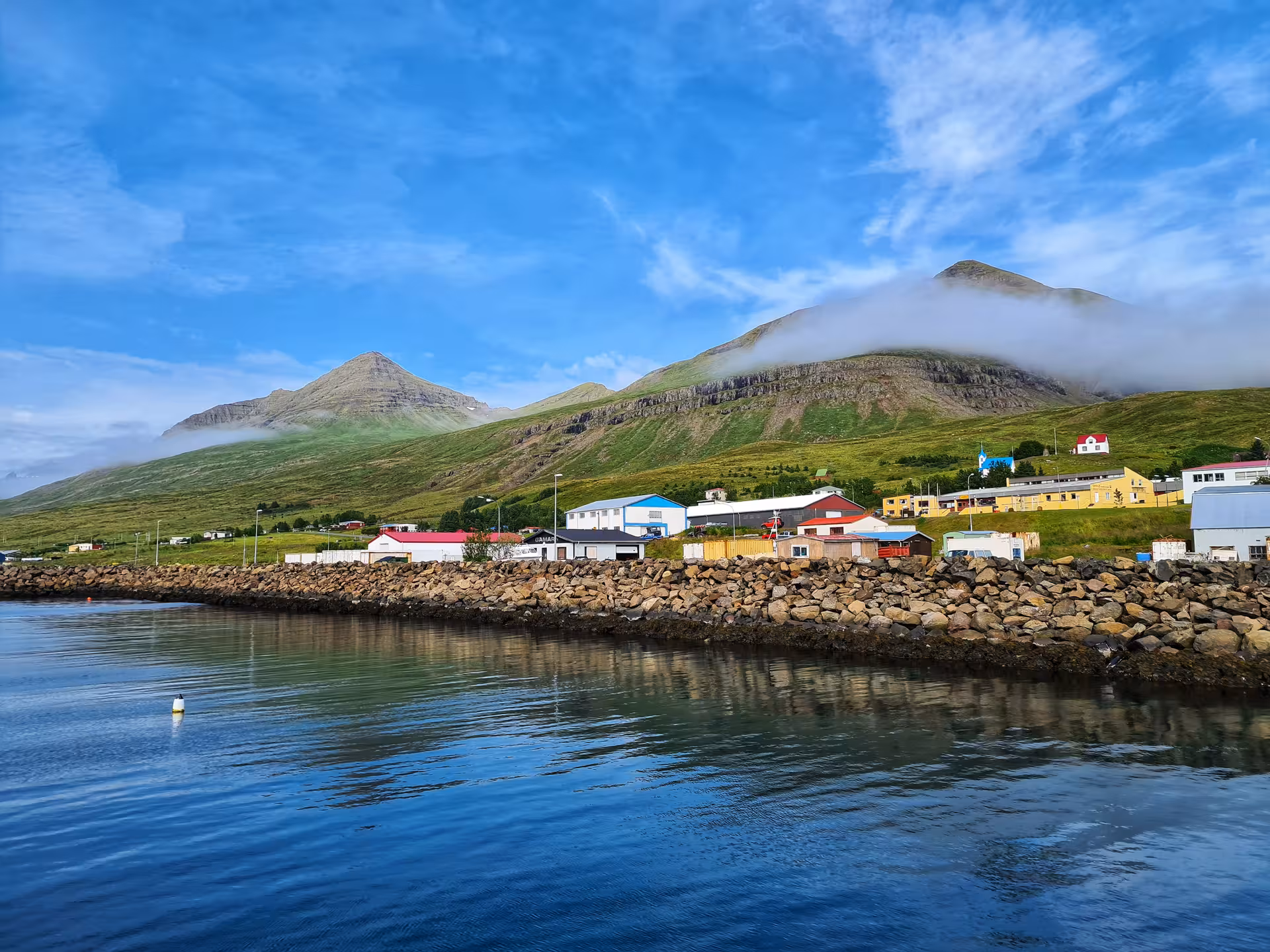 Colorful Icelandic village along a rocky harbor with green mountains and low clouds in the background