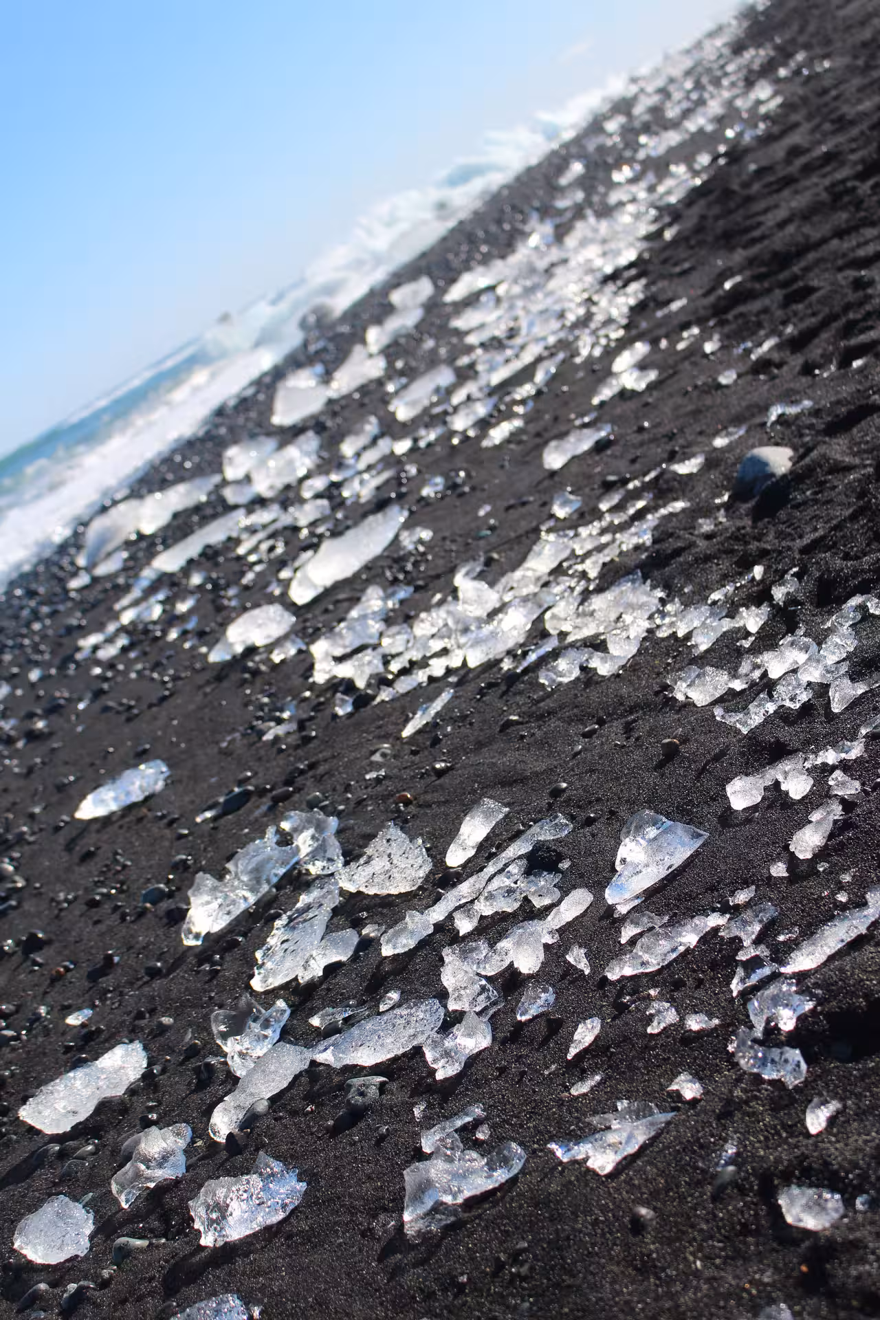 Sparkling ice chunks scattered on black volcanic sand beach in Iceland with ocean waves in background