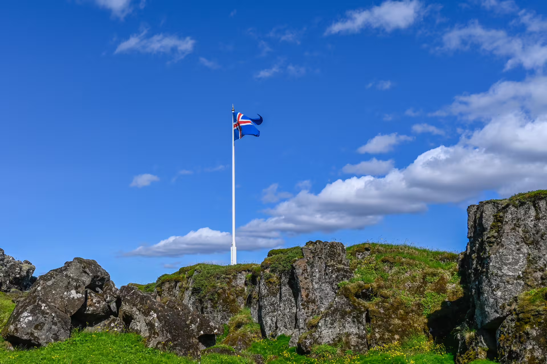Icelandic flag flying over mossy lava rock formations under a blue sky in Iceland