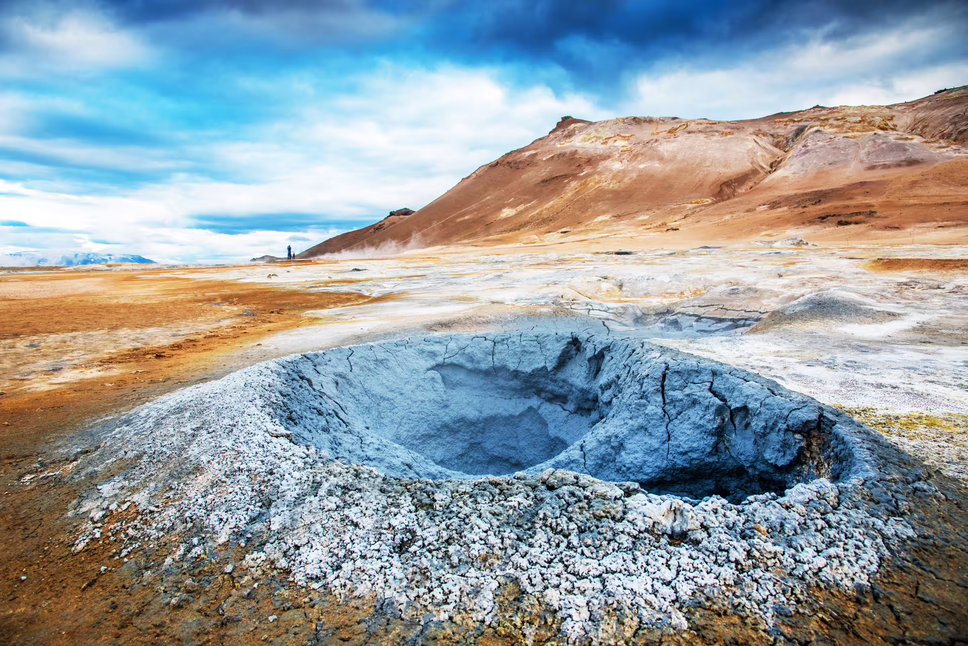 Steaming geothermal mud pool crater at Hverir with volcanic rhyolite mountains in Iceland highlands
