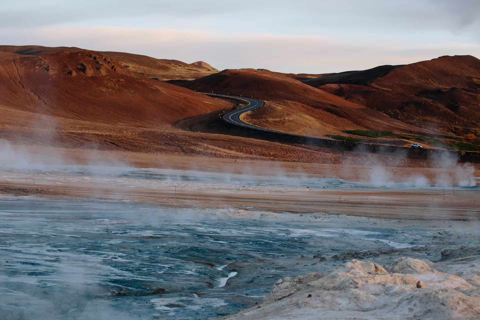 Geothermal steam vents and winding road through red volcanic hills on Iceland Ring Road