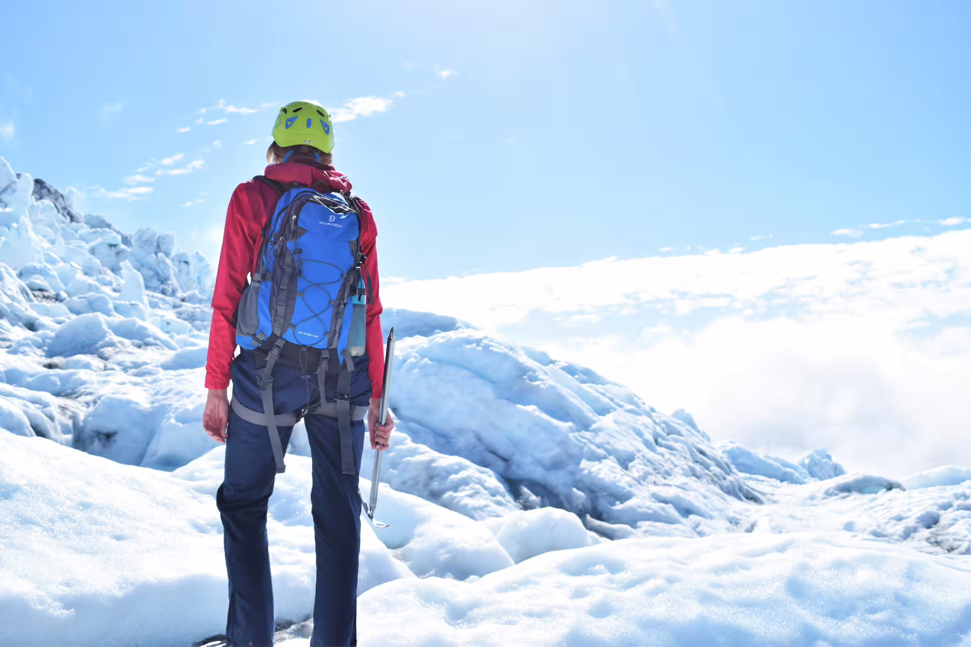 Hiker with ice axe and blue backpack standing on Iceland glacier during ring road tour