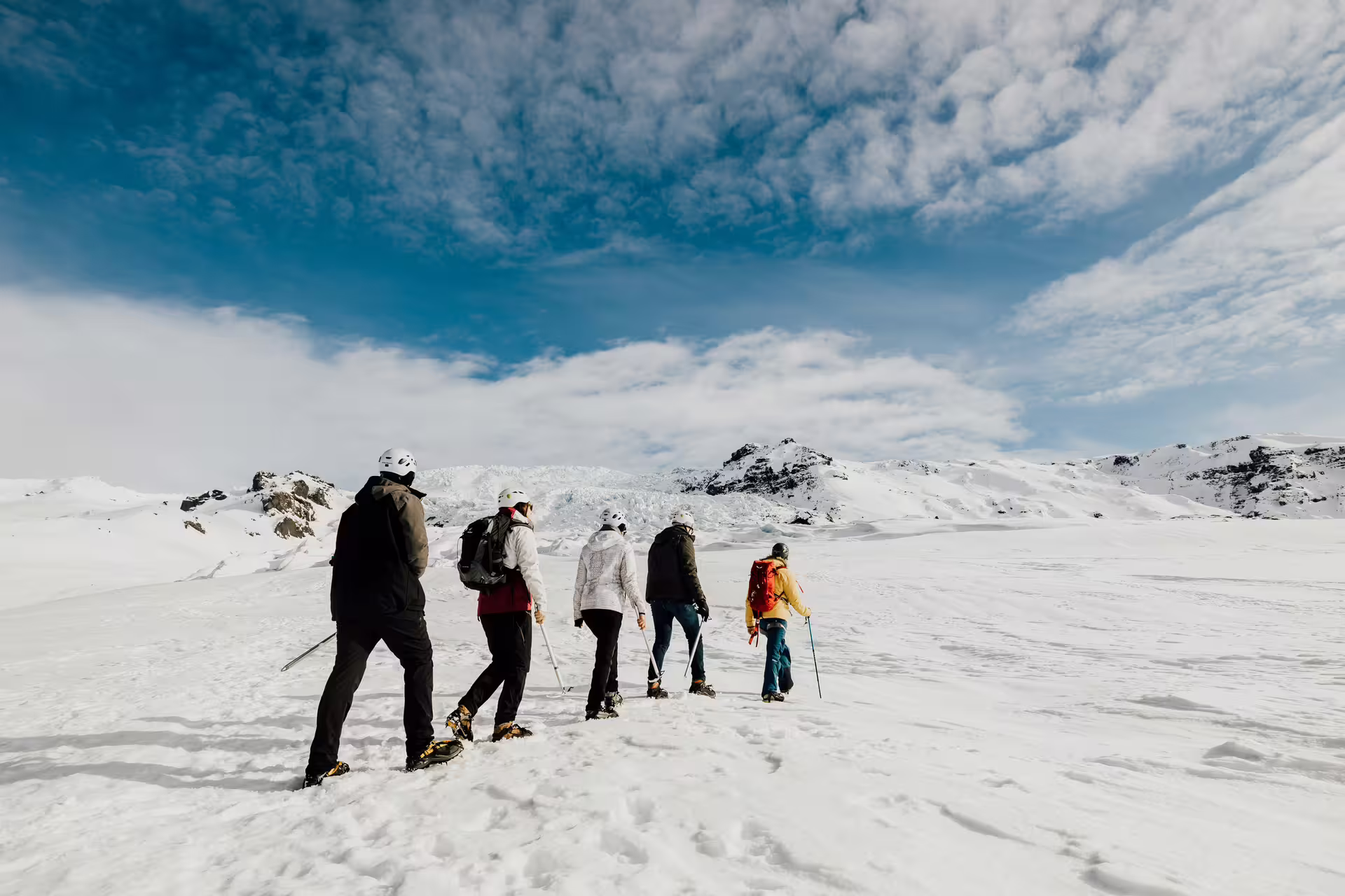 Group of hikers with crampons and helmets trekking across a snowy glacier in Iceland under blue skies