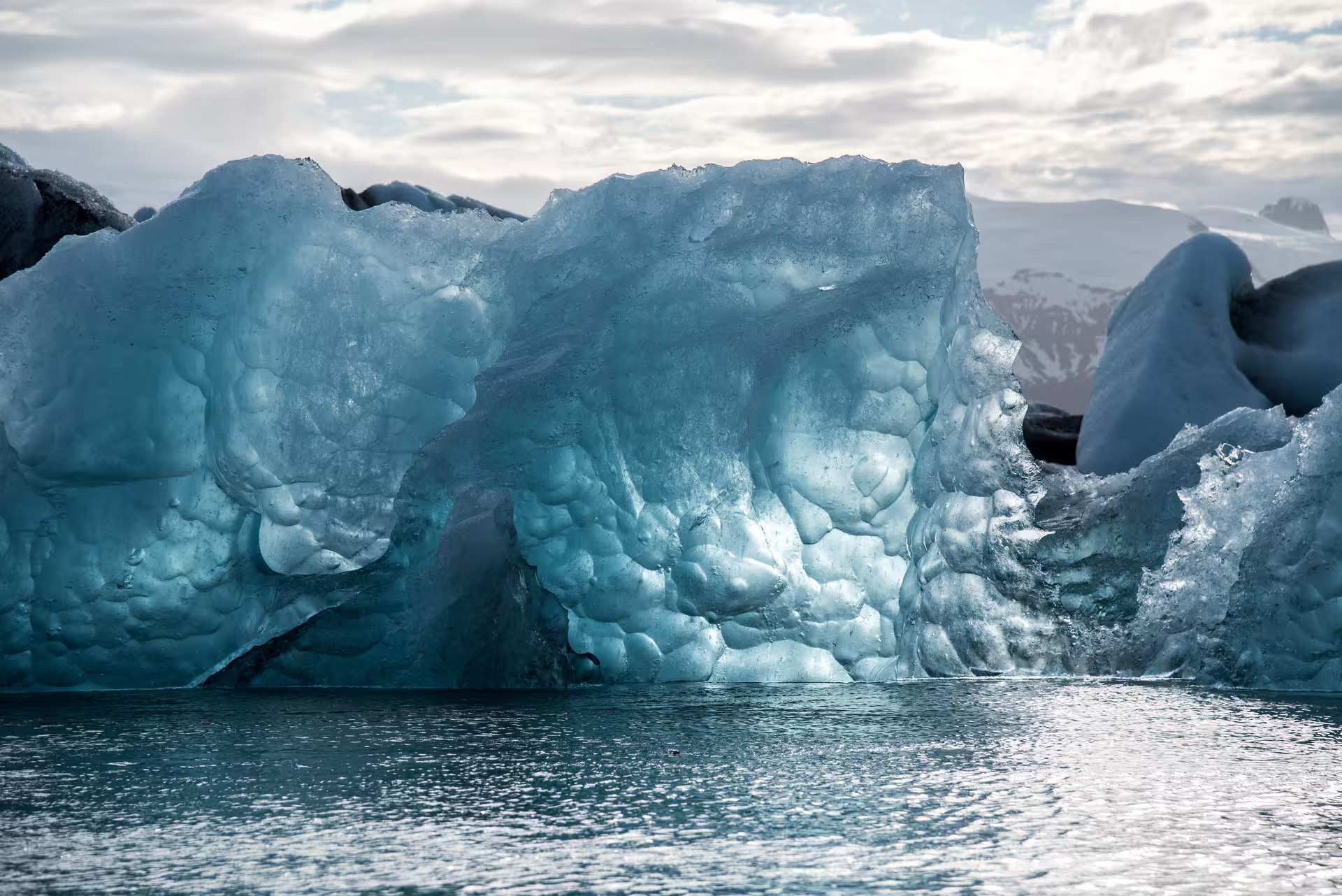 Blue glacial icebergs floating on calm water with snow-capped mountains in Iceland