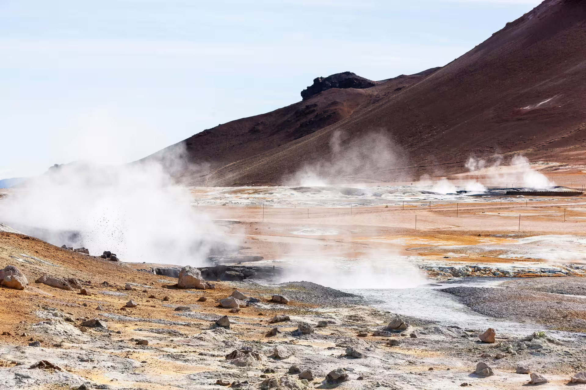 Steaming geothermal vents and mud pools at Hverir with a red volcanic mountain in Iceland