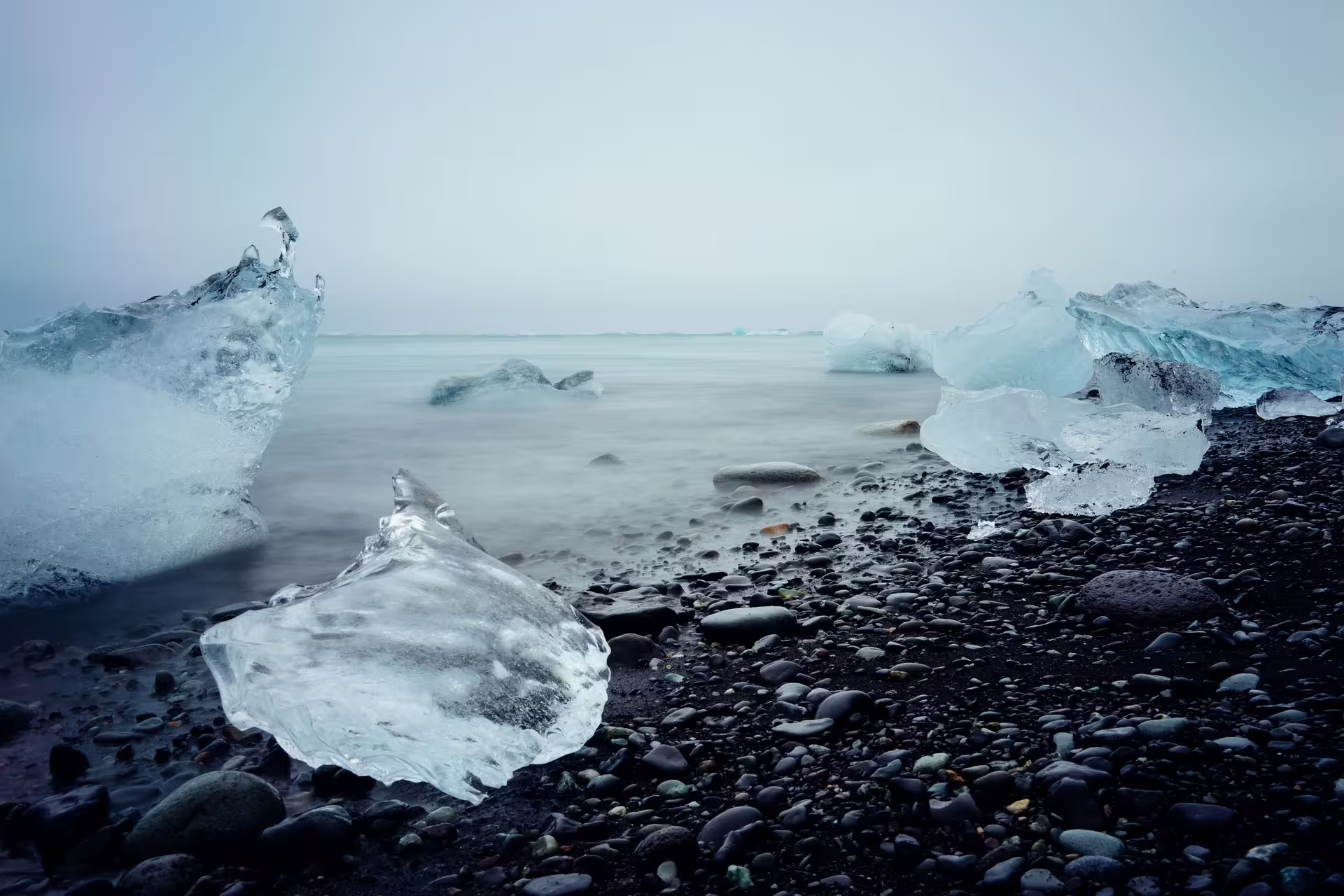 Ice chunks on black volcanic pebble beach with misty Arctic ocean in Iceland