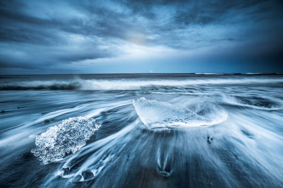 Ice chunks on black sand beach with misty waves and dramatic stormy sky in Iceland