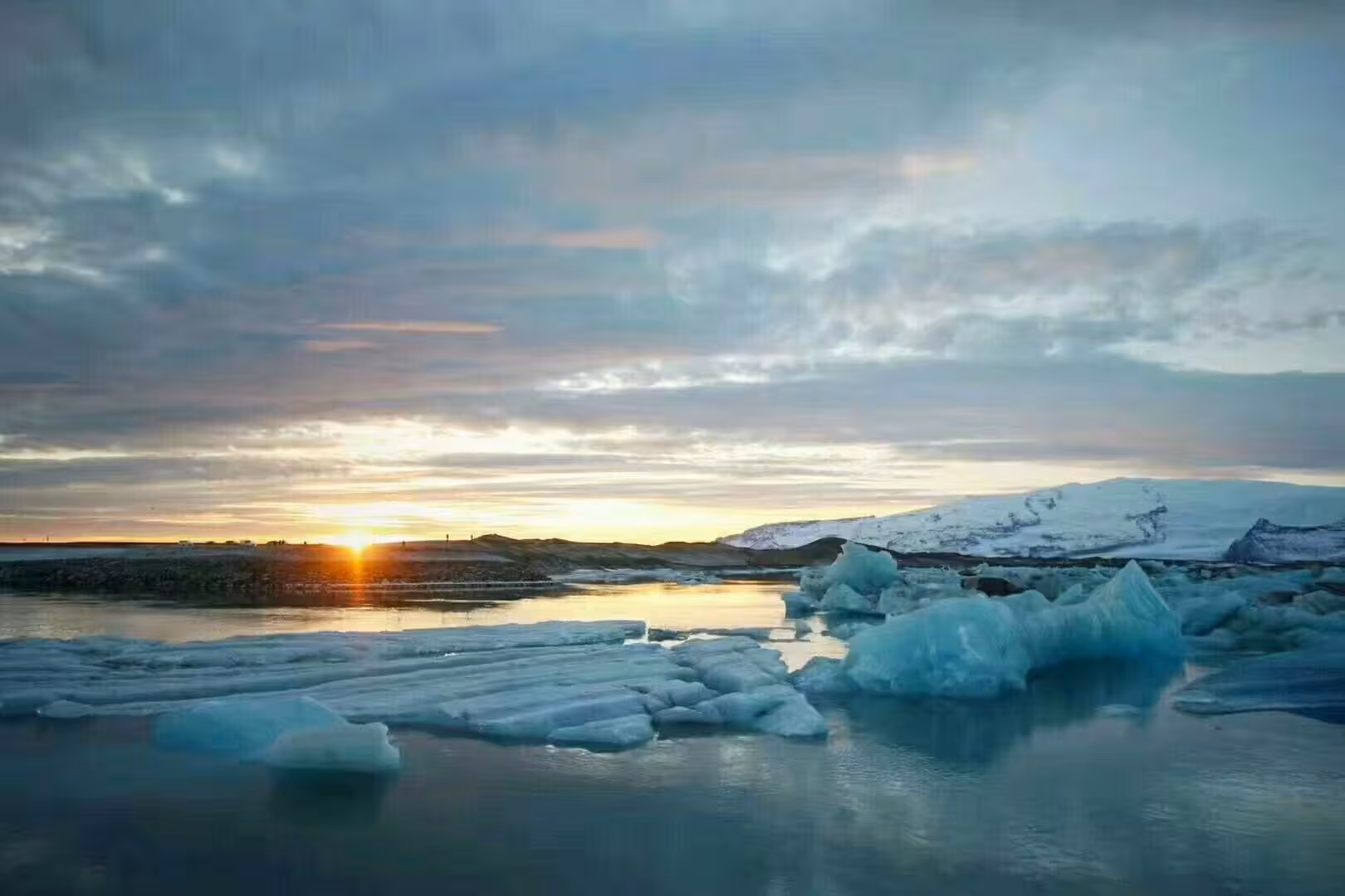 Turquoise icebergs floating on Jokulsarlon glacier lagoon at sunset with snow-capped mountains in Iceland