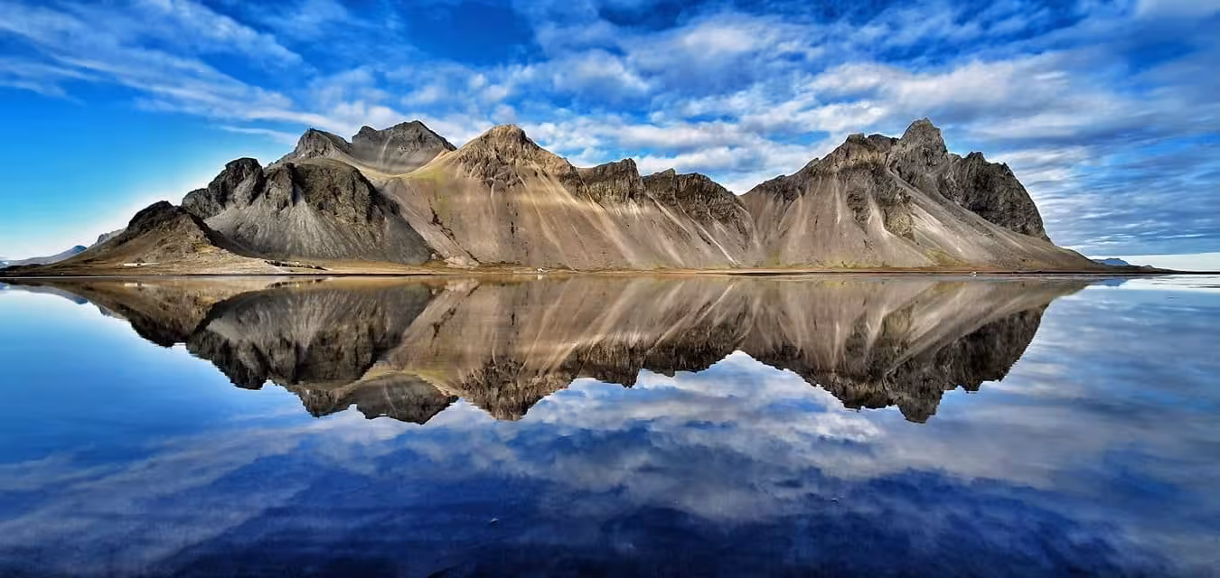 Dramatic Icelandic mountain range perfectly reflected in still glacial waters under a vivid blue sky