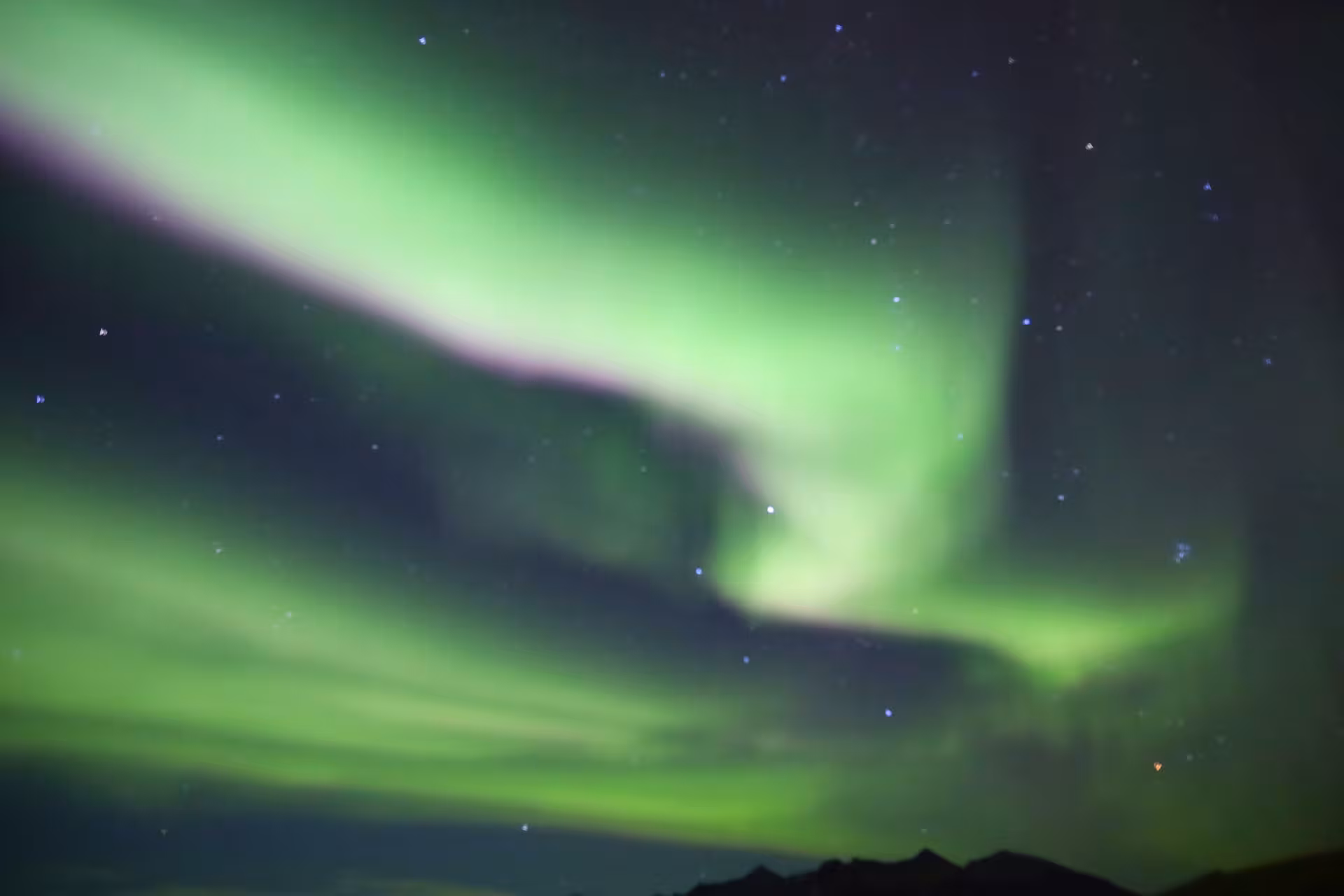 Vibrant green and purple northern lights swirling over Iceland mountain silhouettes at night