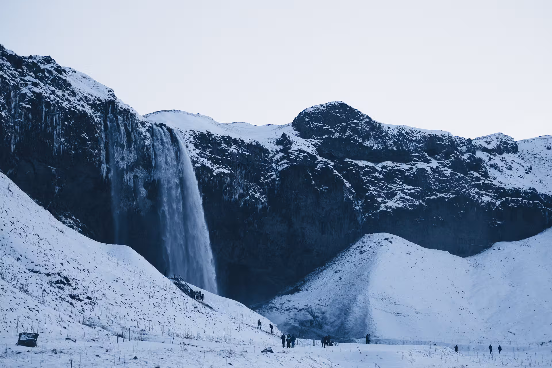 Seljalandsfoss waterfall cascading down snow-covered cliffs in Iceland with tourists in foreground