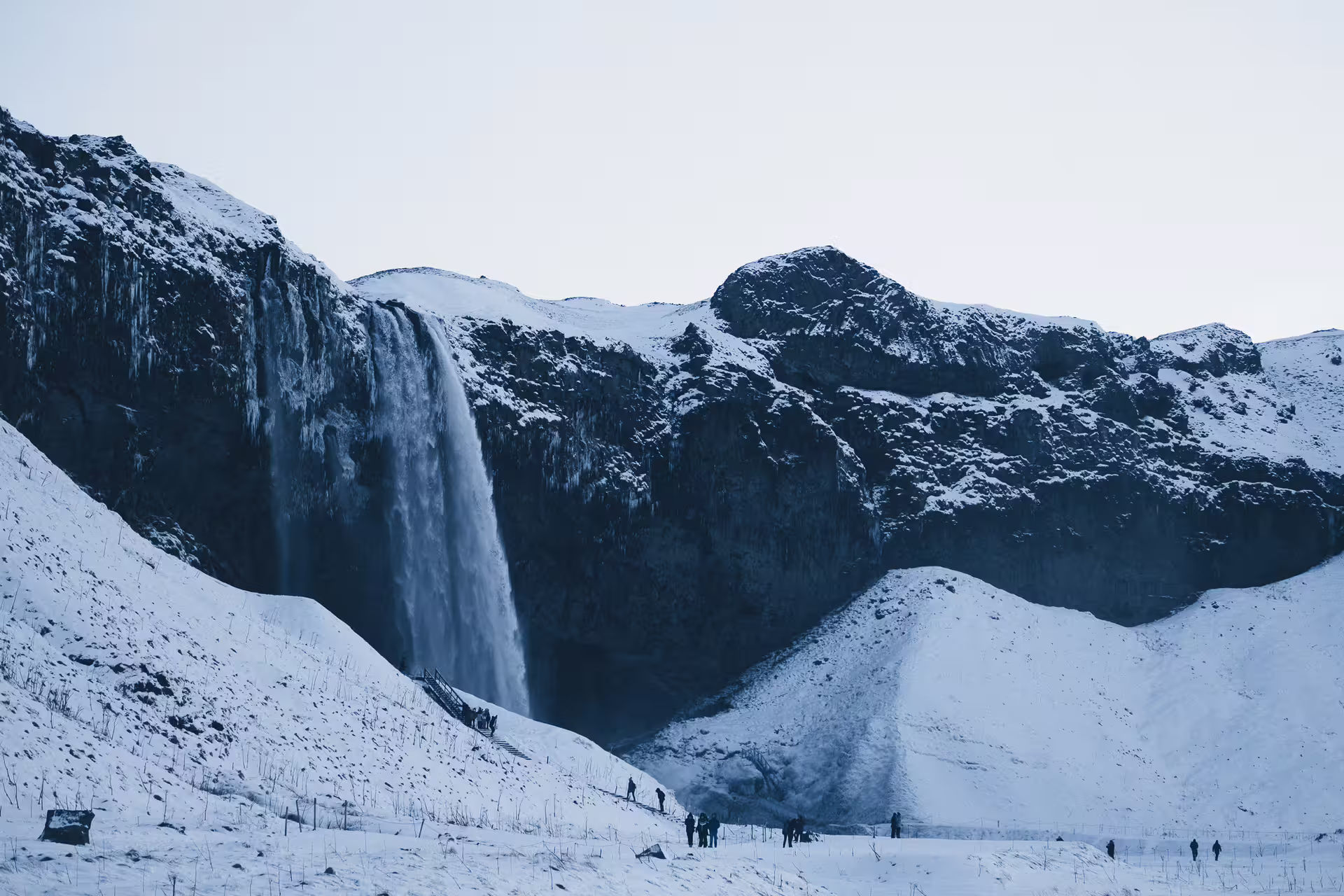 Seljalandsfoss waterfall in winter with snow-covered cliffs and tourists on Iceland Ring Road