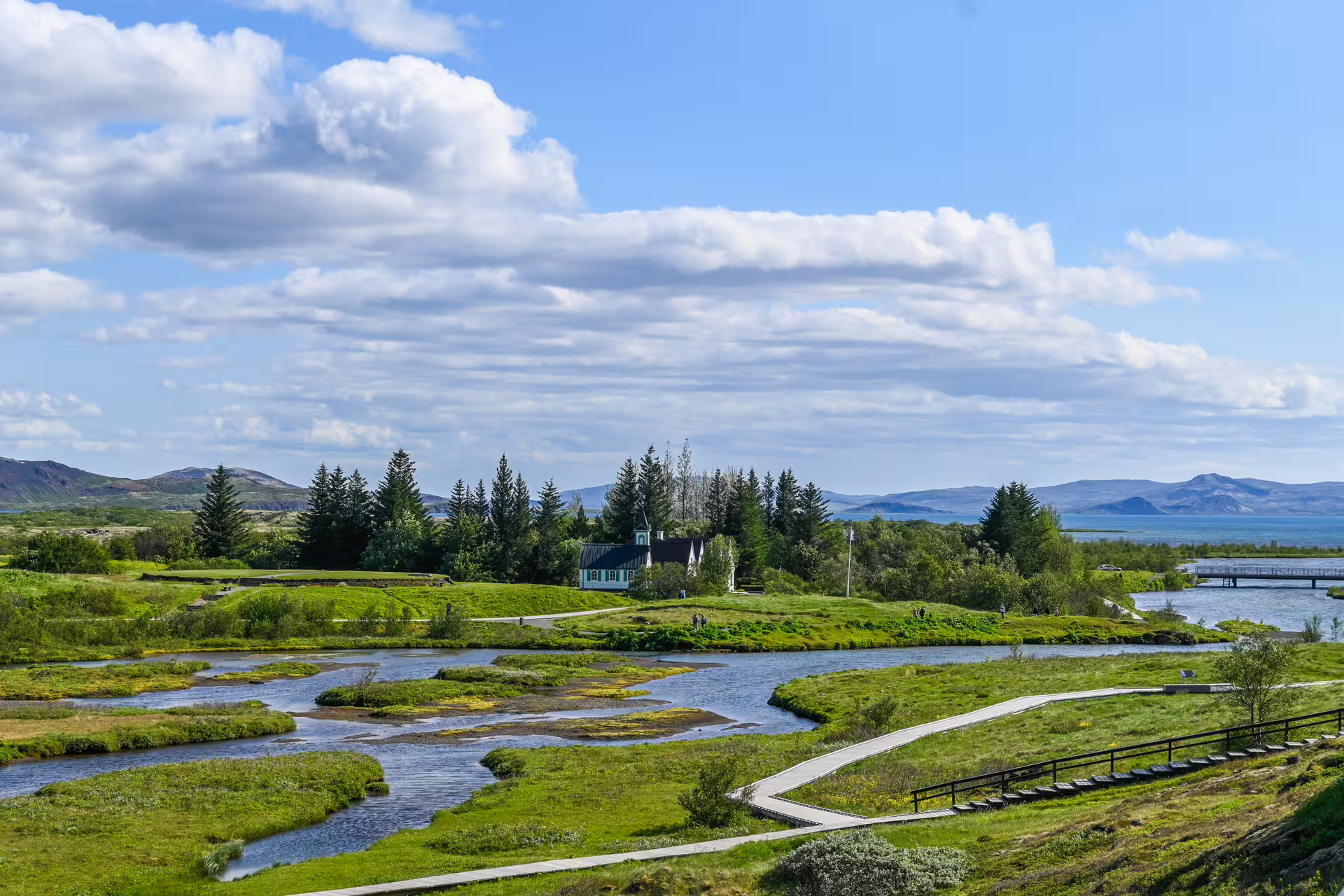Scenic Þingvellir National Park with winding river, green meadows, church, and mountains in Iceland