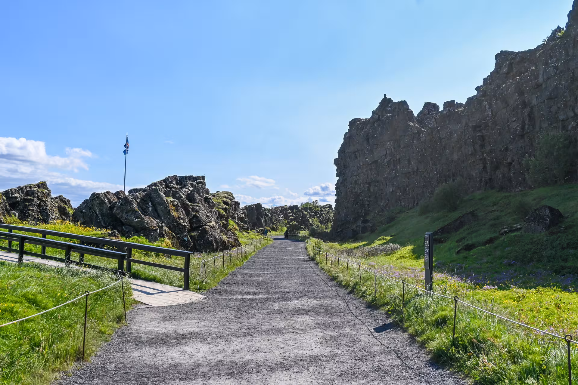 Gravel walking path through Þingvellir rift valley with Icelandic flag and jagged lava rock walls