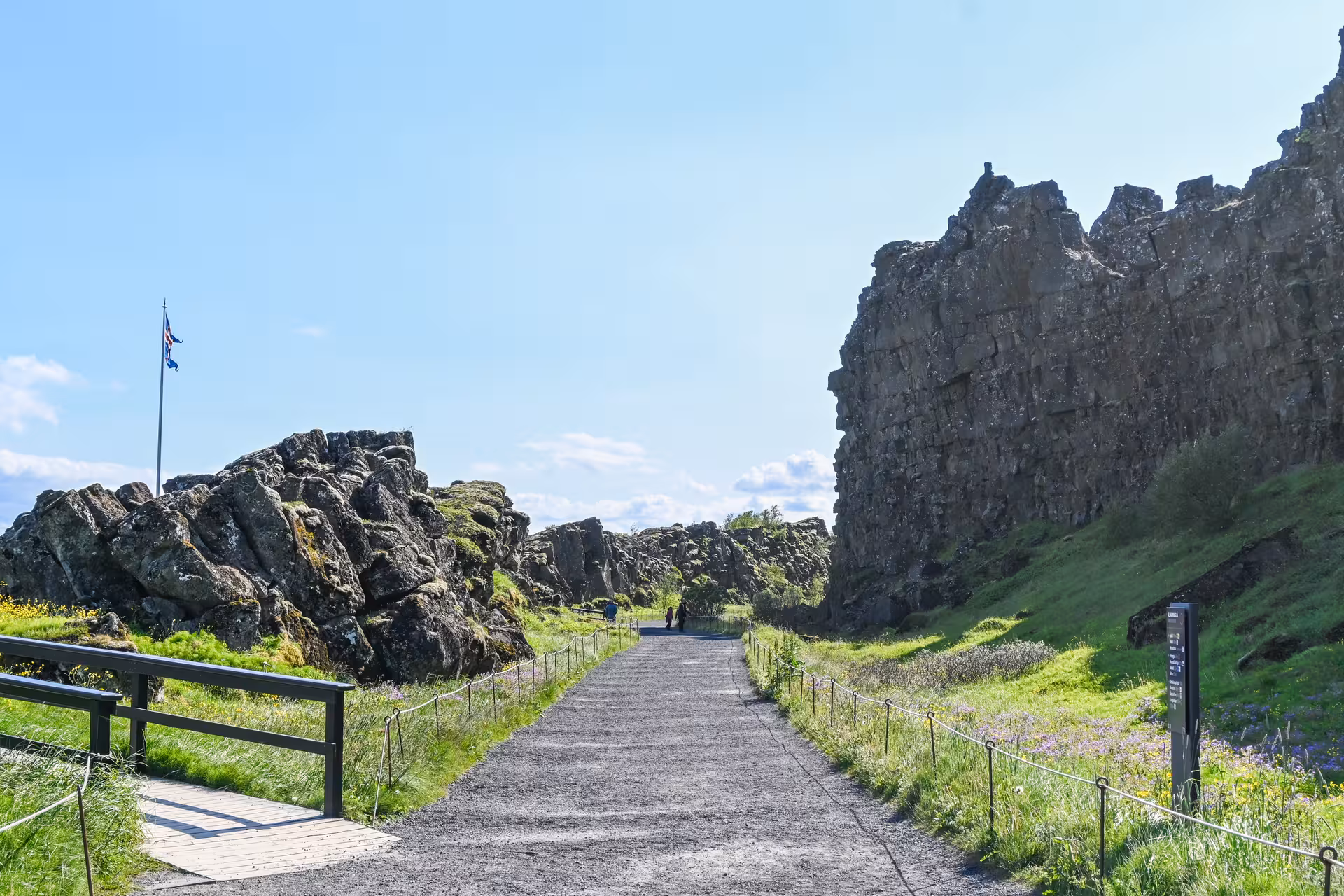 Gravel path through volcanic rock formations at Þingvellir National Park, Iceland, with Icelandic flag on sunny day