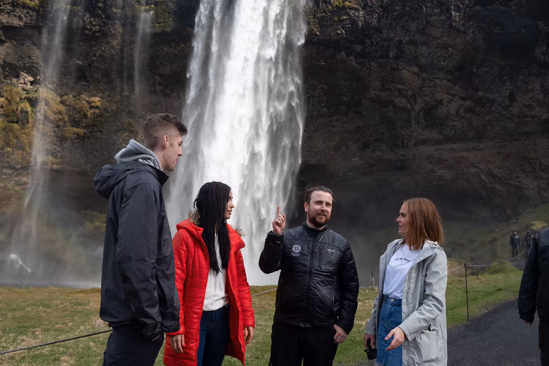 Tour guide pointing at Seljalandsfoss waterfall in Iceland with group of tourists