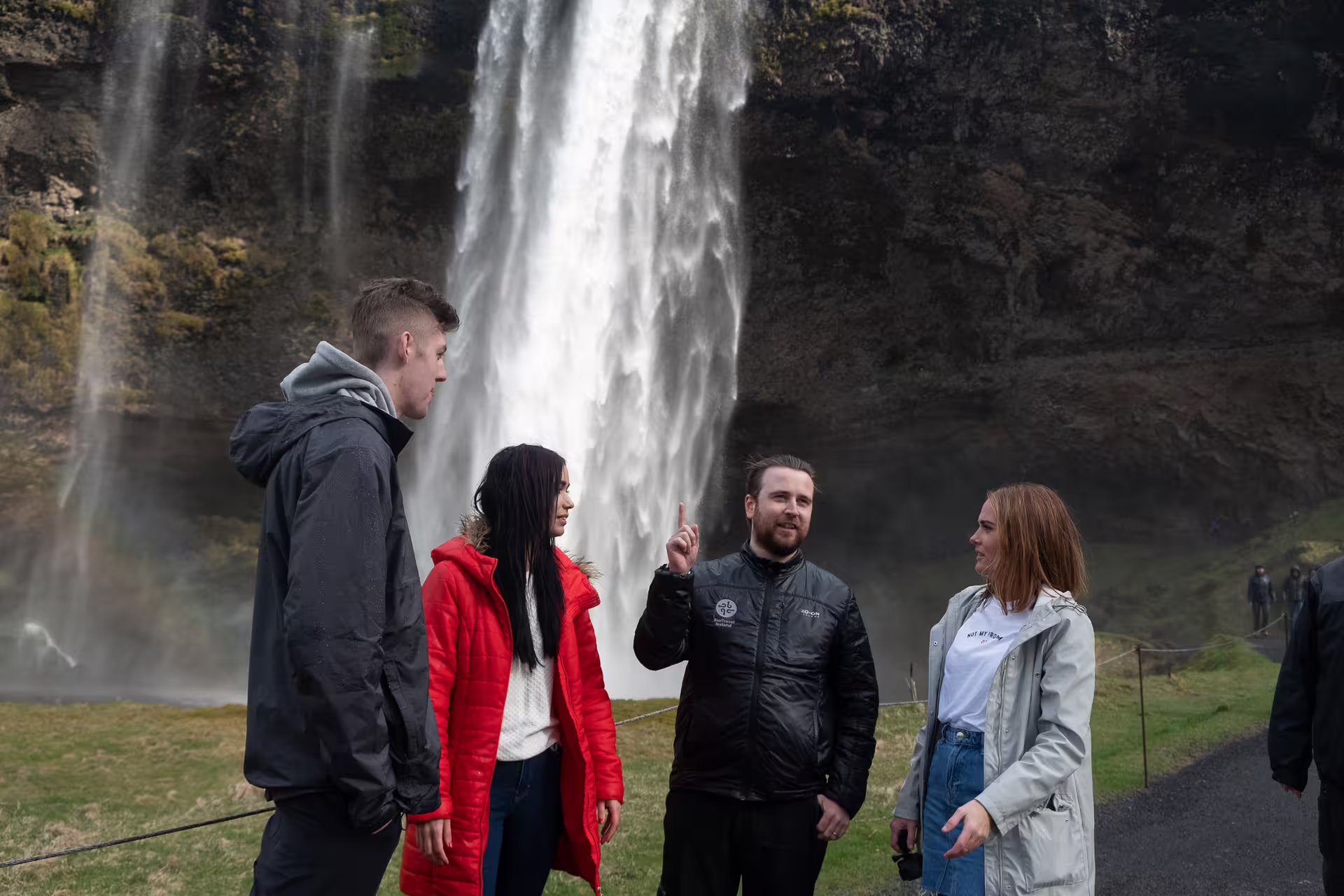 Tour guide pointing at Seljalandsfoss waterfall in Iceland with group of tourists on Ring Road tour