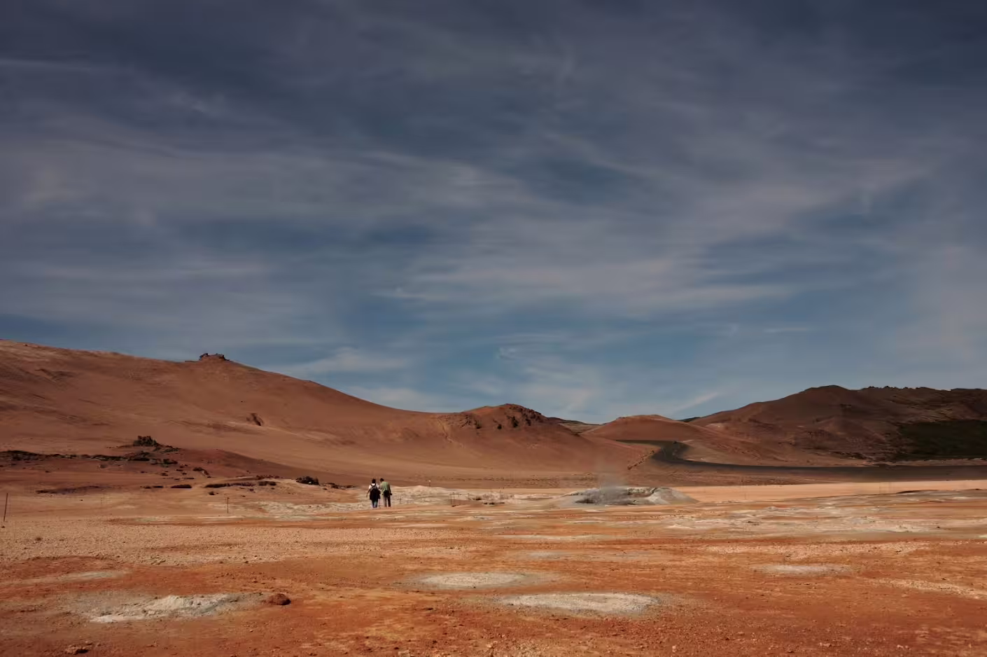 Two hikers walking across vast red volcanic landscape with rust-colored hills in Iceland