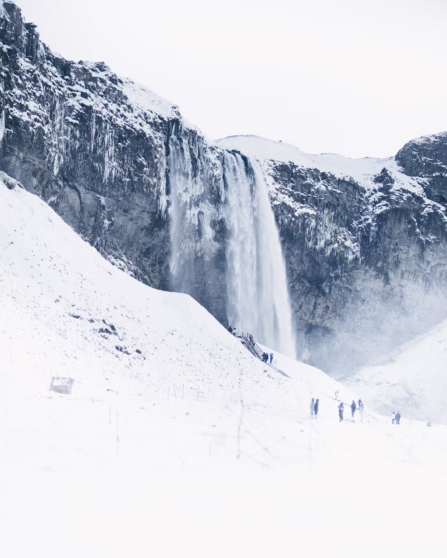 Seljalandsfoss waterfall in winter with snow-covered cliffs and tourists on Iceland Ring Road tour