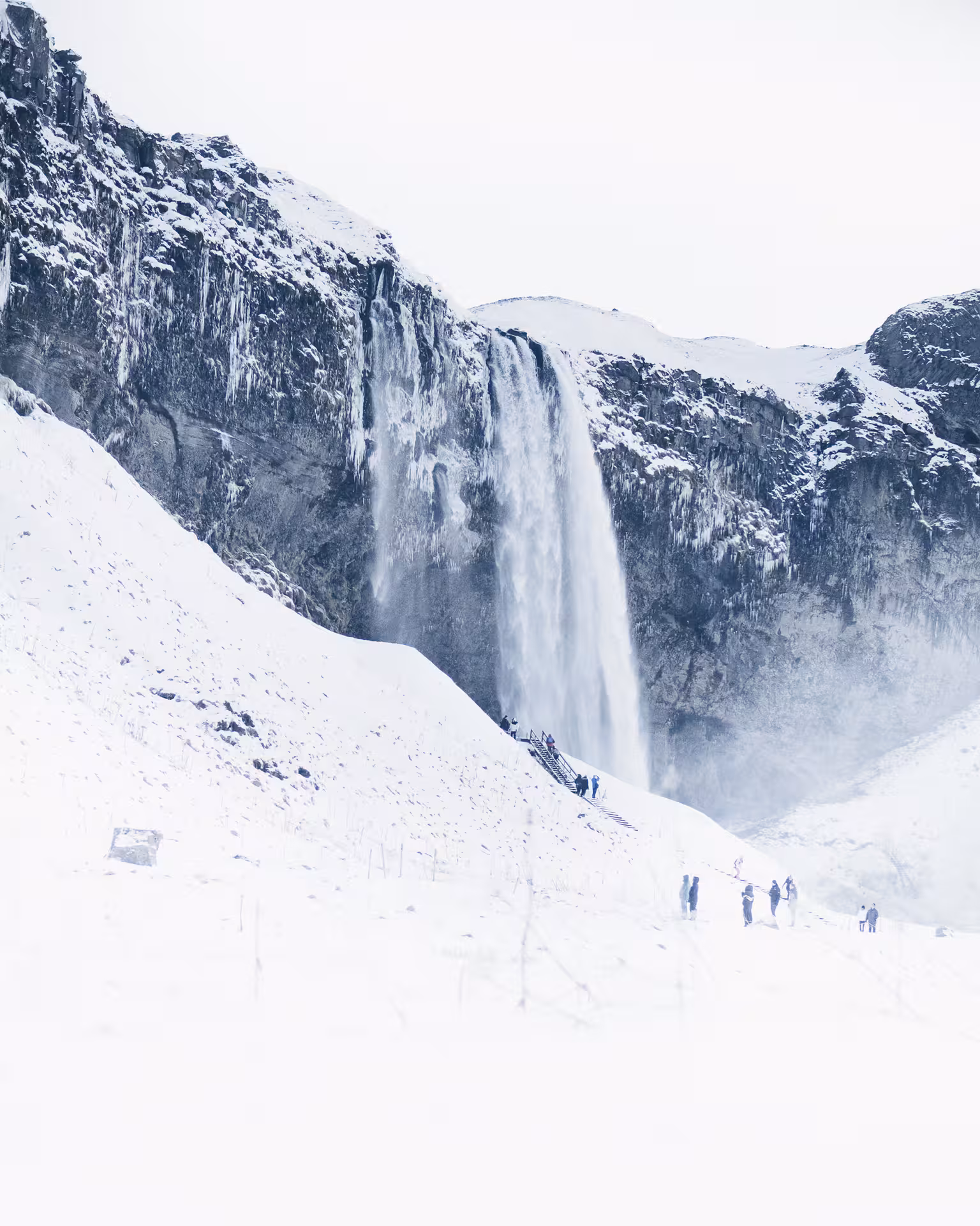 Seljalandsfoss waterfall cascading down snow-covered cliffs in Iceland with tourists in foreground