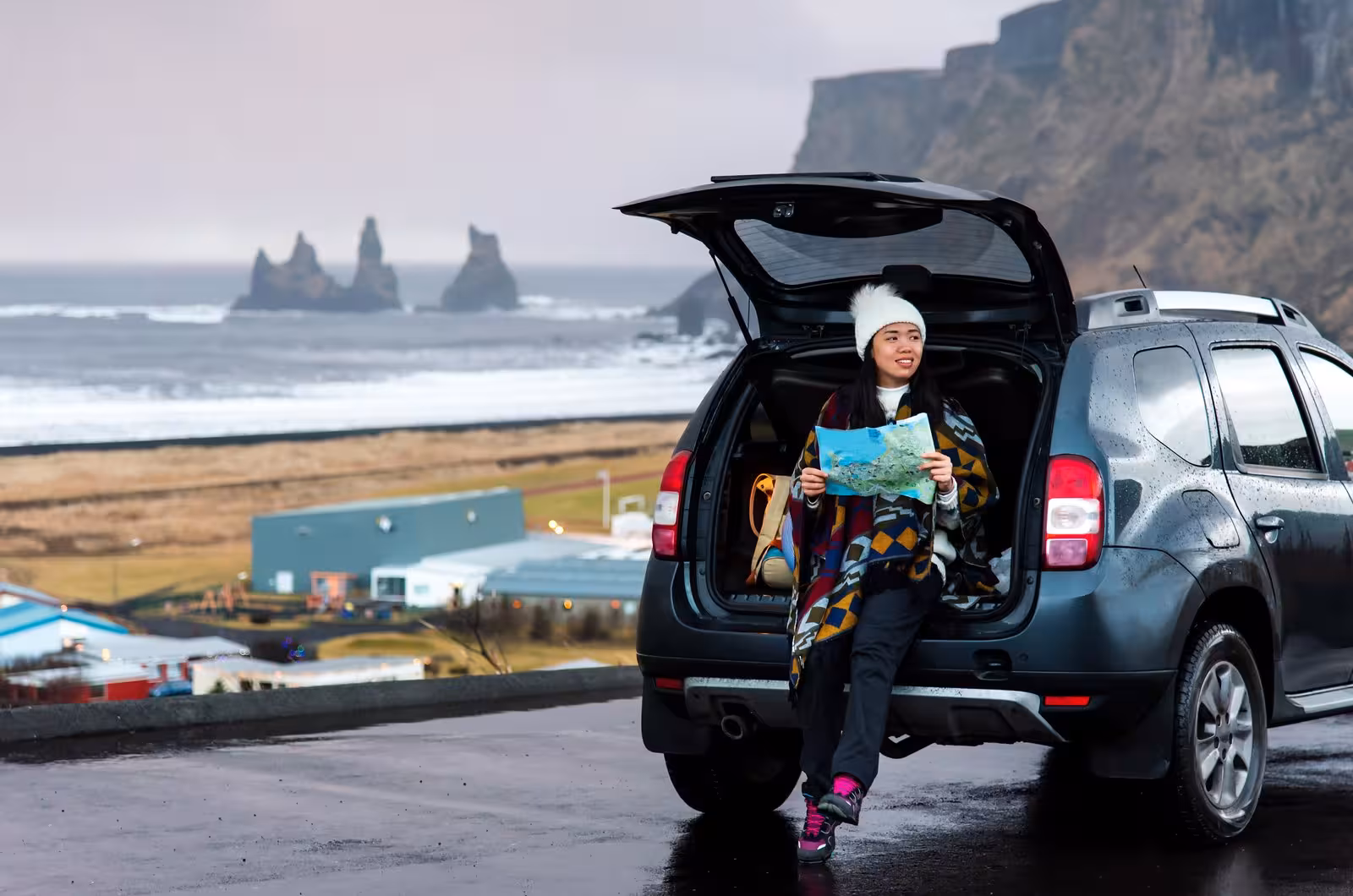 Tourist with a map sitting in a car trunk, enjoying the scenic views of Iceland's Reynisfjara beach during a road trip.