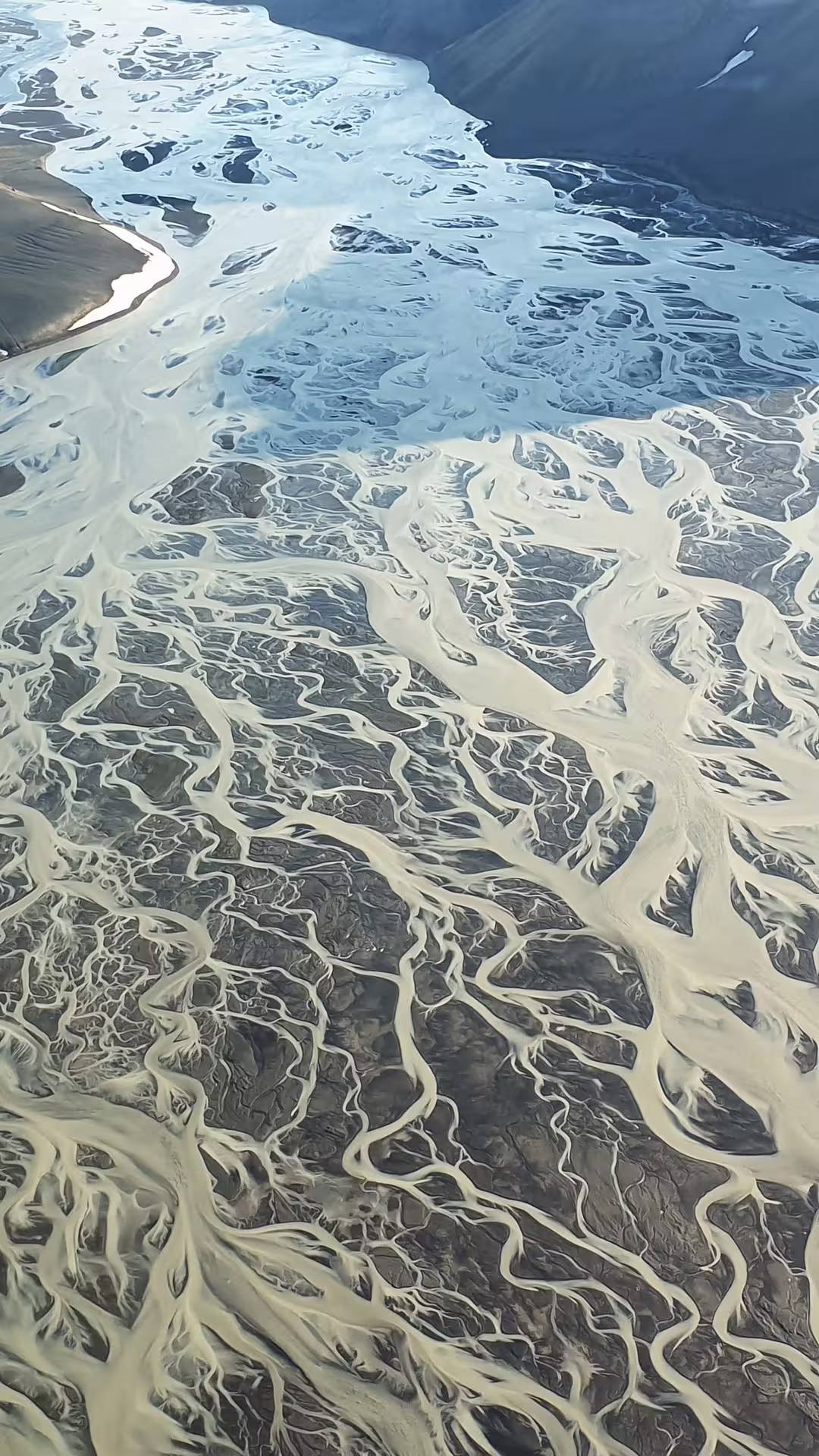 Aerial view of braided glacial river delta with sandy channels flowing toward blue water in Iceland