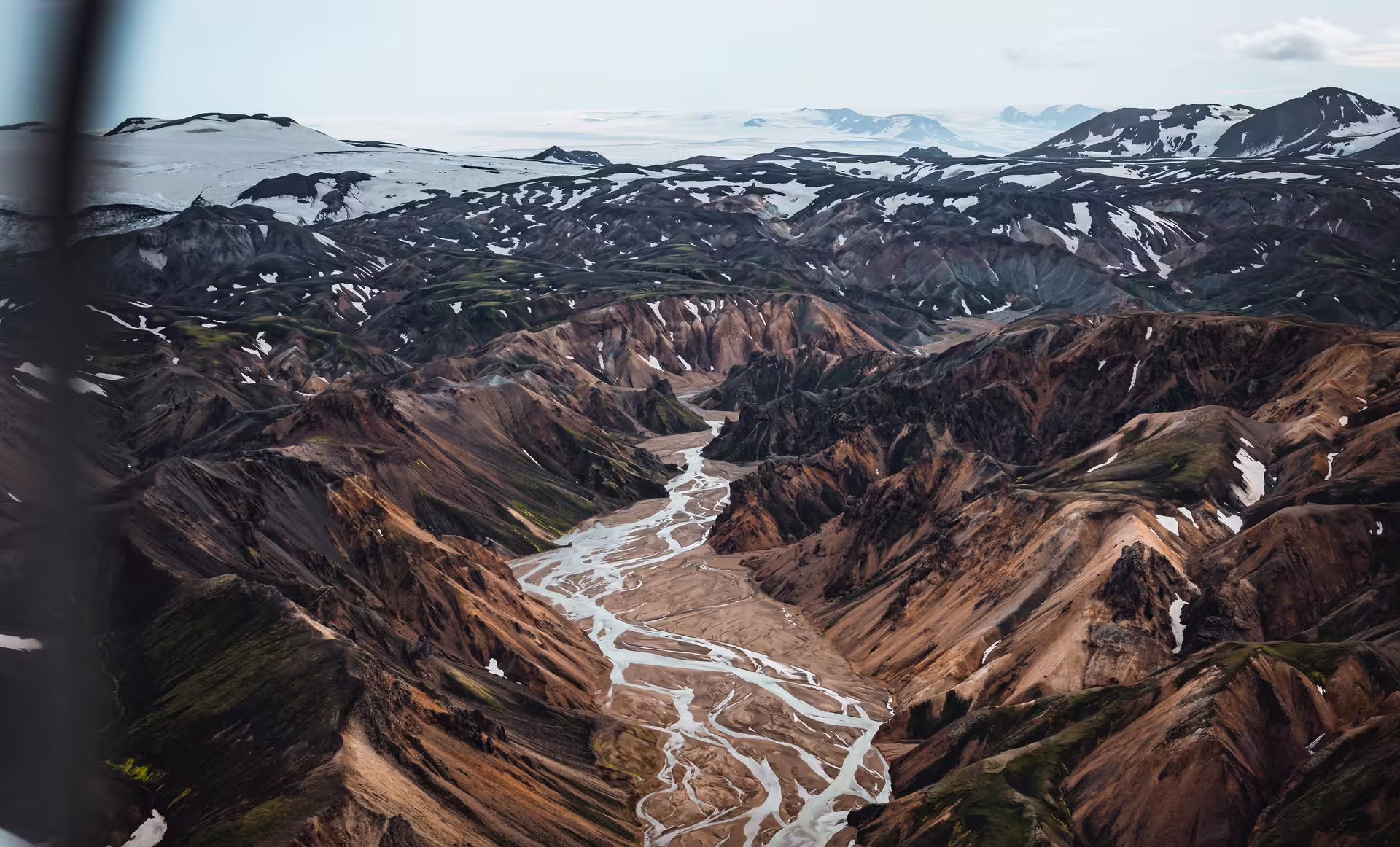 Aerial view of braided glacial river winding through rugged Icelandic highlands with snow-capped mountains