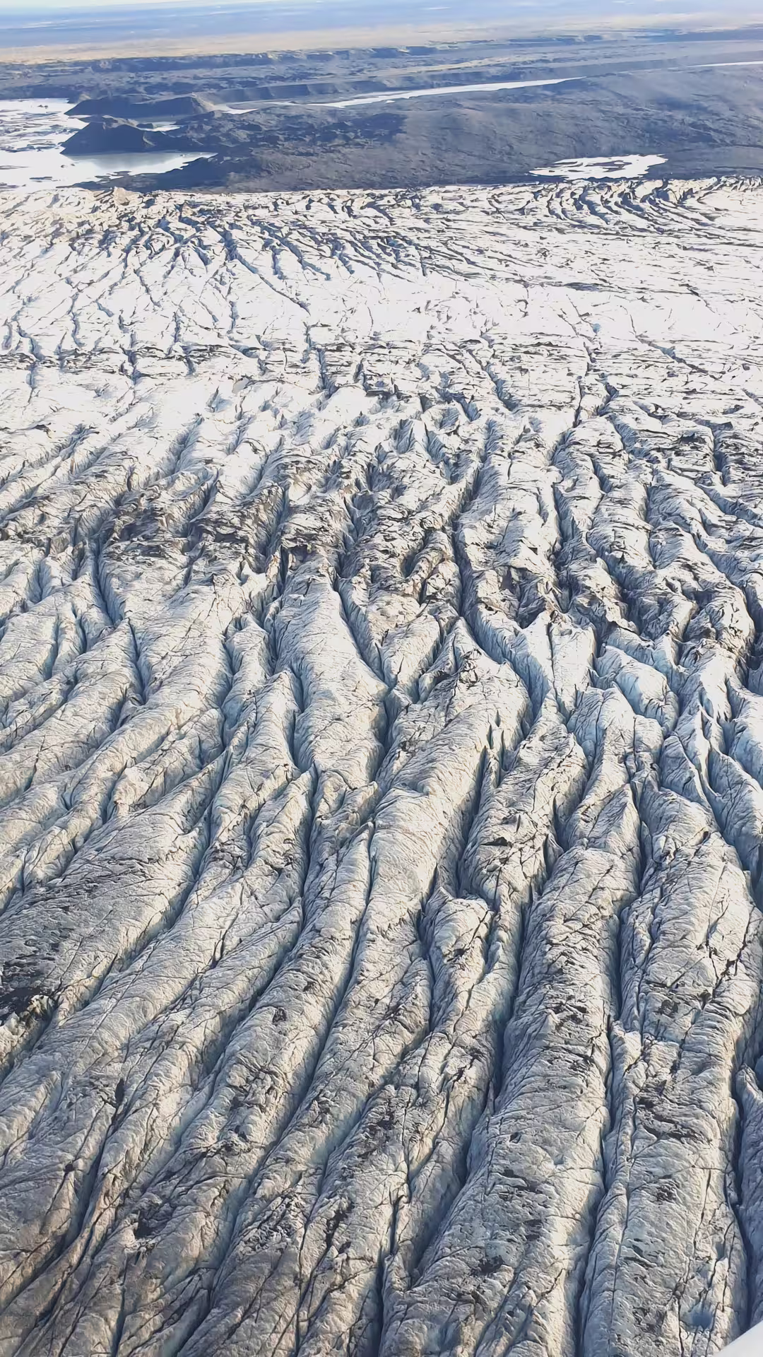 Aerial view of heavily crevassed glacier ice field in Iceland with volcanic landscape in background