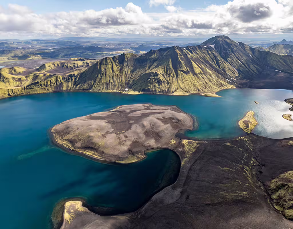 Aerial view of a volcanic crater lake with turquoise water and green mountains in Iceland