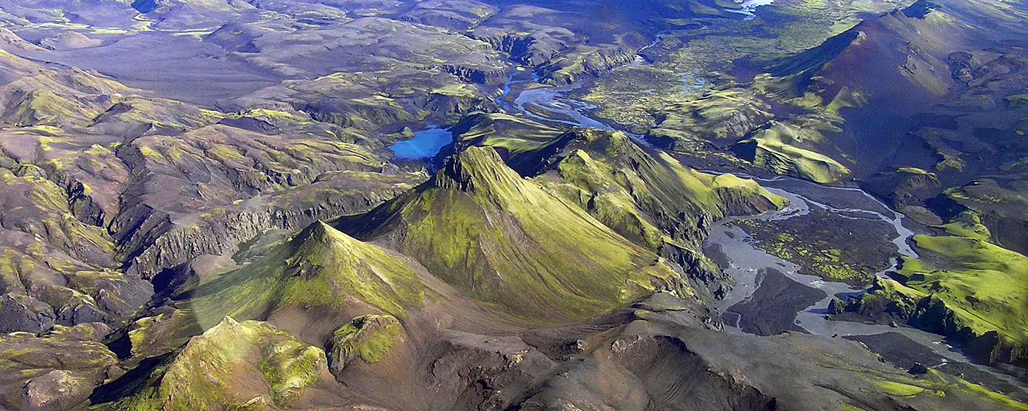 Aerial view of moss-covered volcanic mountains and winding glacial rivers in Iceland's highland wilderness