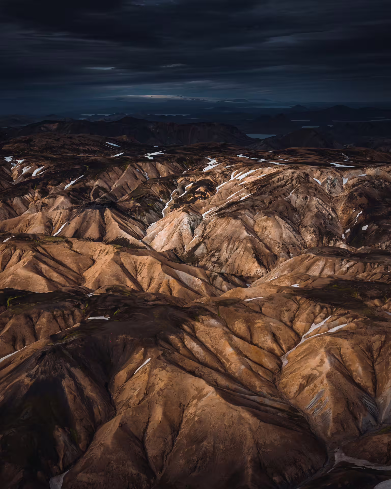 Aerial view of rugged volcanic highlands with snow patches under dramatic dark sky in Iceland