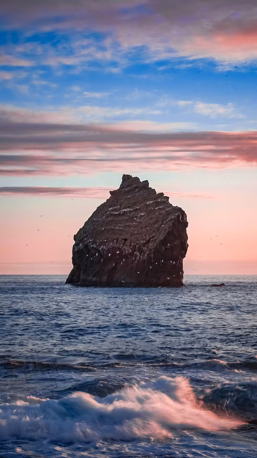 Dramatic sea stack rising from ocean waves at sunset during Iceland Super Jeep adventure tour