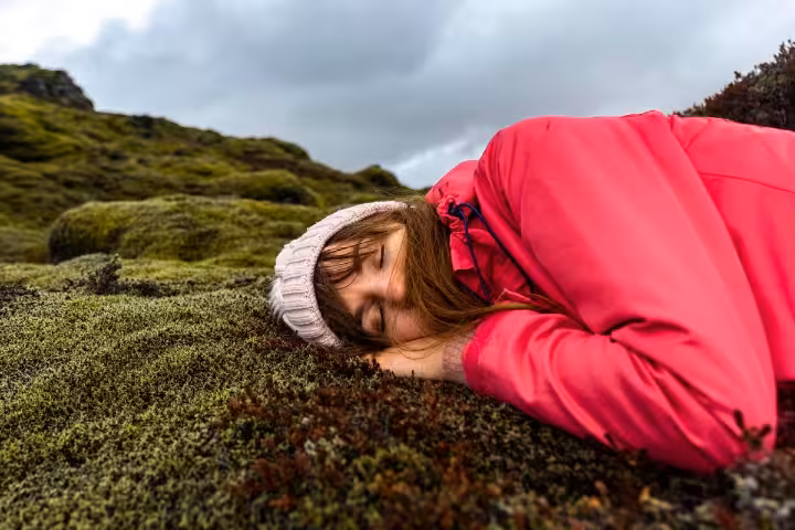 Traveler in pink jacket resting on lush Icelandic moss, capturing serene moments on the 12-day self-drive tour.