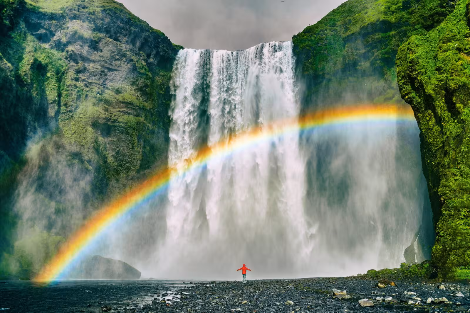 Majestic Skógafoss waterfall with vibrant rainbow and visitor during Iceland self-drive tour.