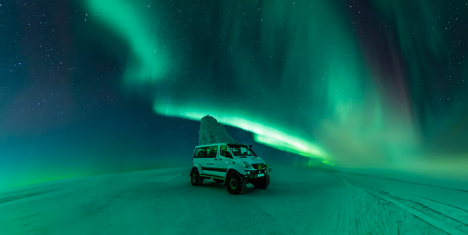4x4 van under vibrant green northern lights on snowy Iceland landscape at night