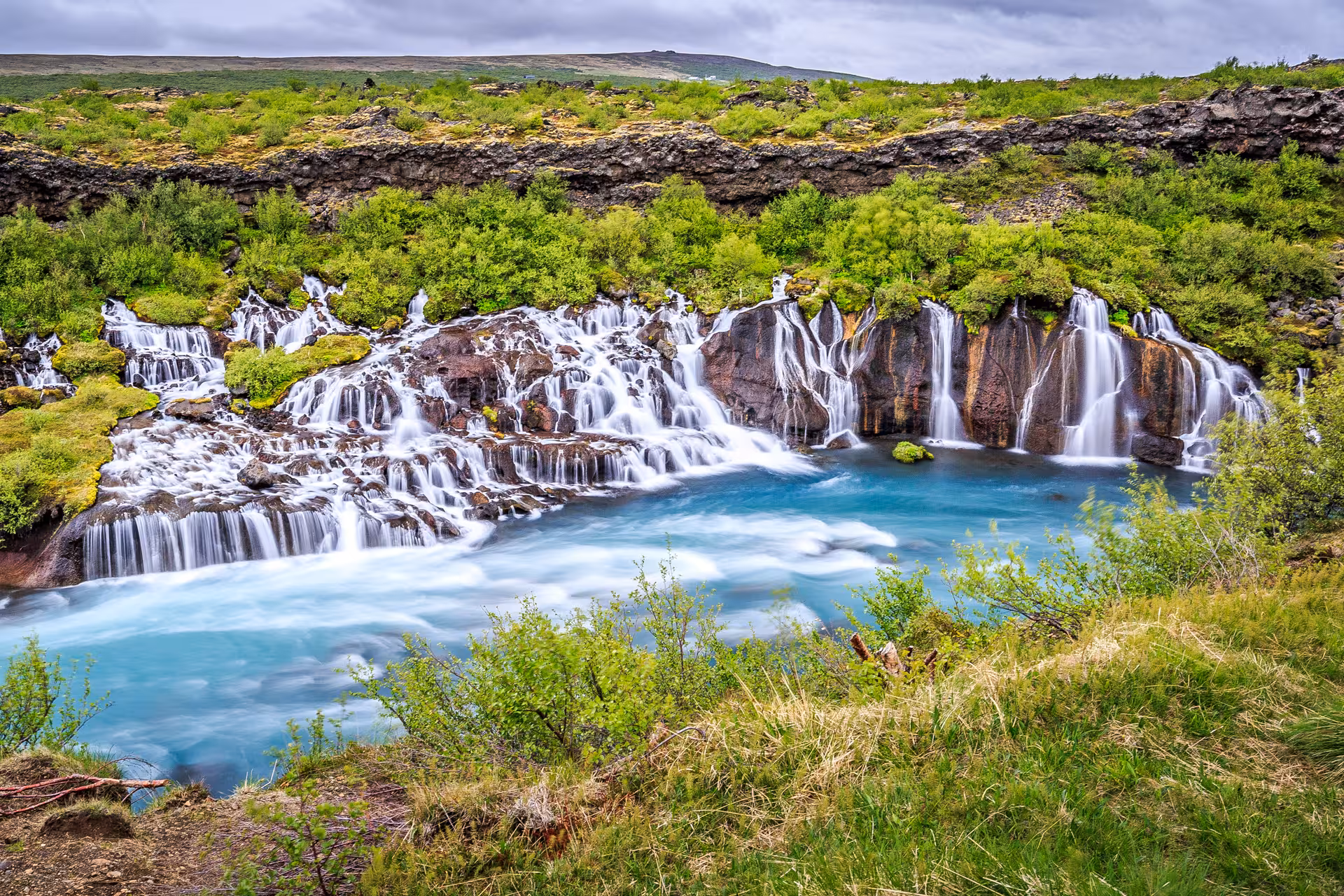 Multiple cascading waterfalls flowing over lava rock into a turquoise river in Iceland's Snaefellsnes region
