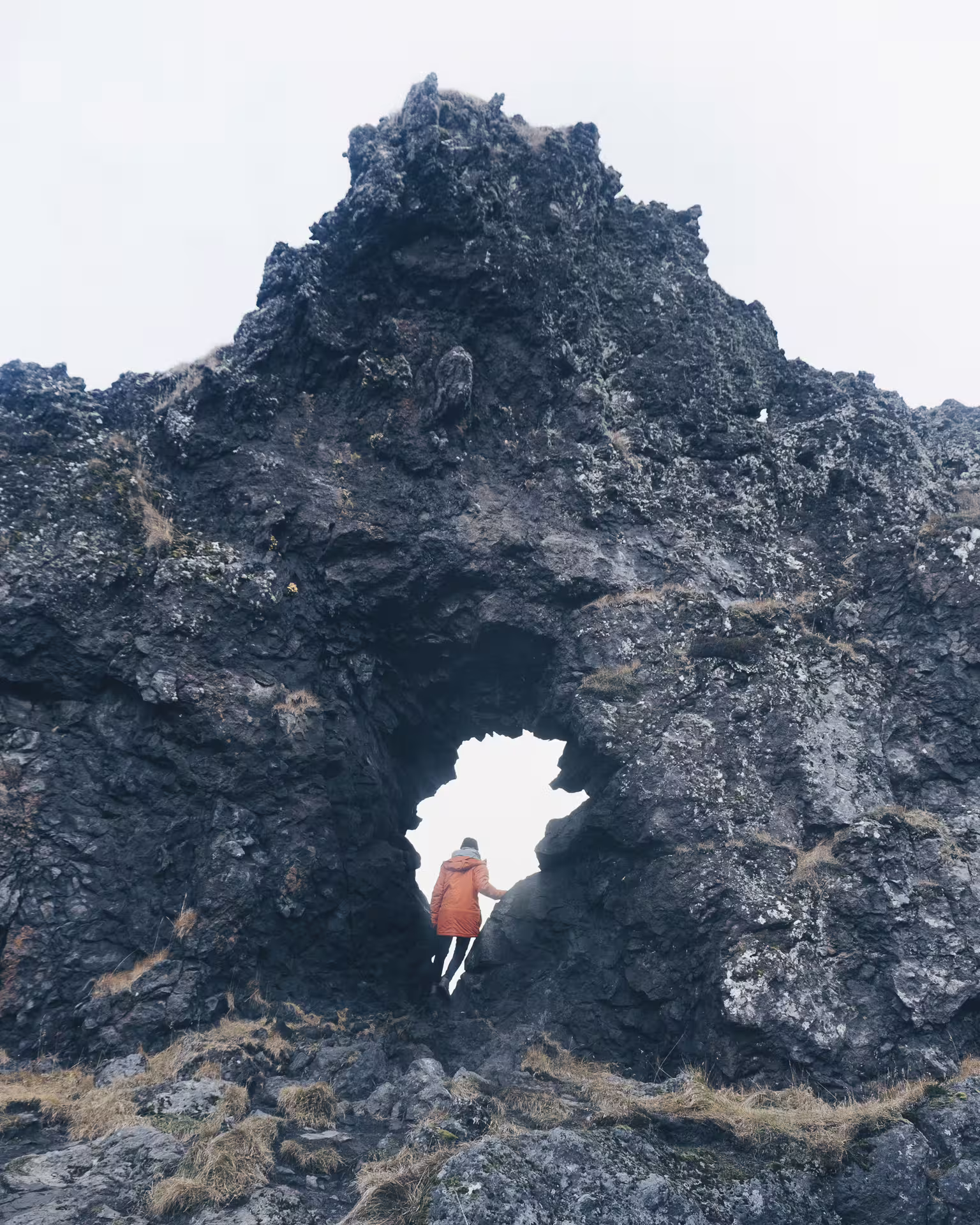 Hiker in orange jacket standing in natural lava rock arch on Iceland's Snæfellsnes Peninsula