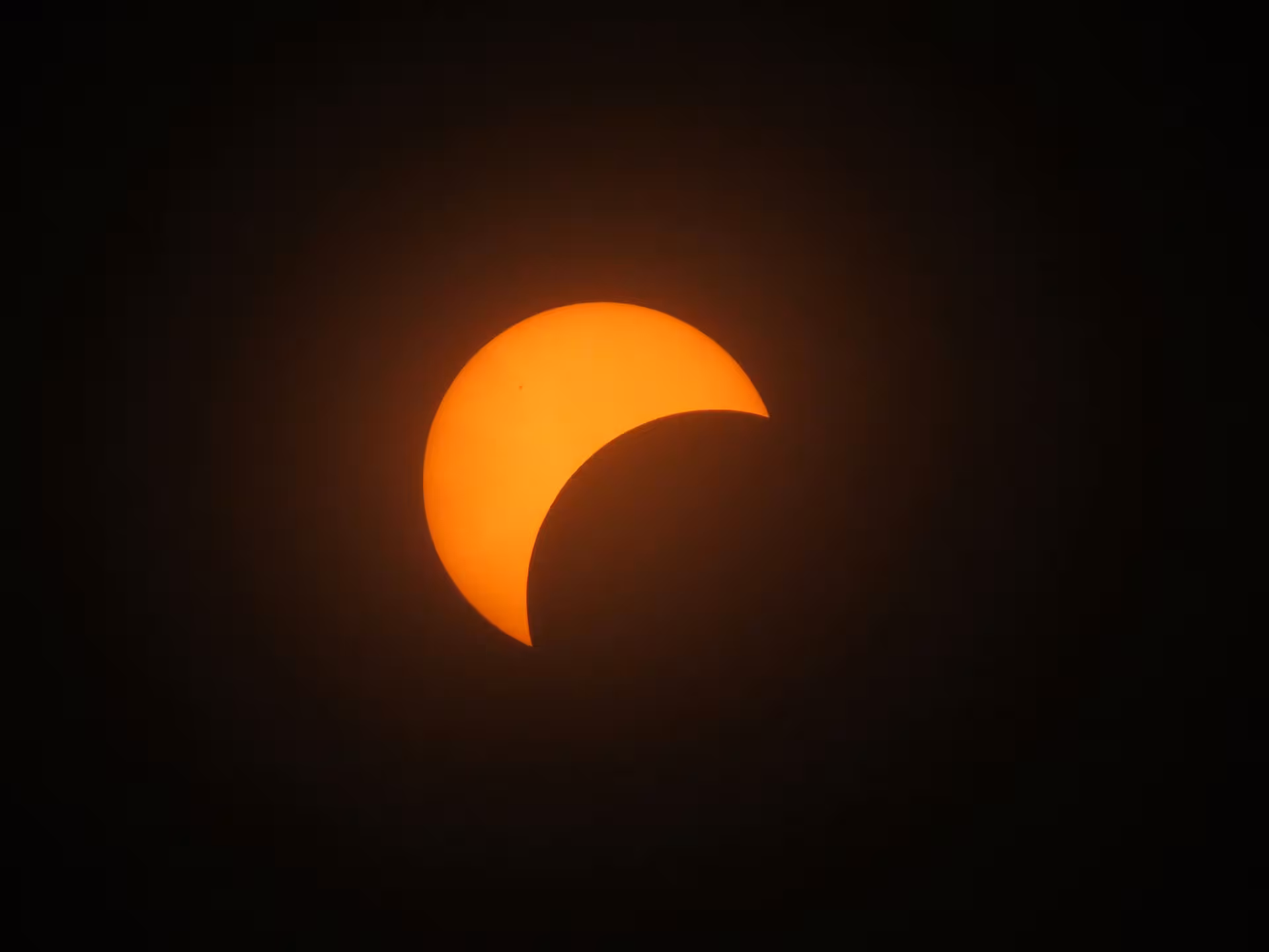 Partial solar eclipse showing crescent sun with moon shadow against dark sky