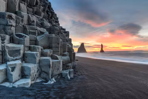 Basalt column cliffs and sea stacks on black sand beach at sunset, Iceland South Coast