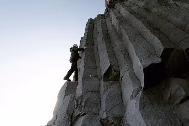 Rock climber scaling dramatic basalt columns on Iceland's south coast cliff face