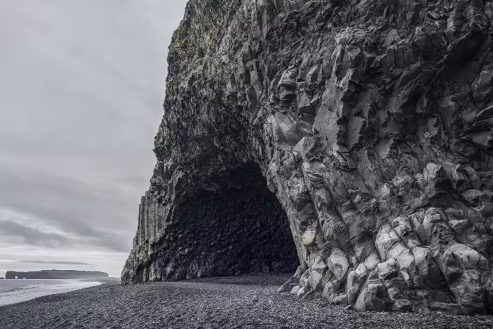 Dark basalt sea cave arch on Iceland's black sand south coast beach under overcast skies