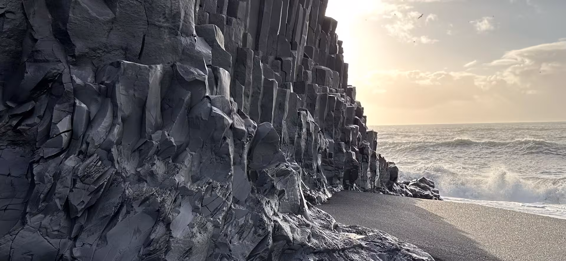 Towering black basalt columns meet black sand beach with crashing Atlantic waves on Iceland's South Coast
