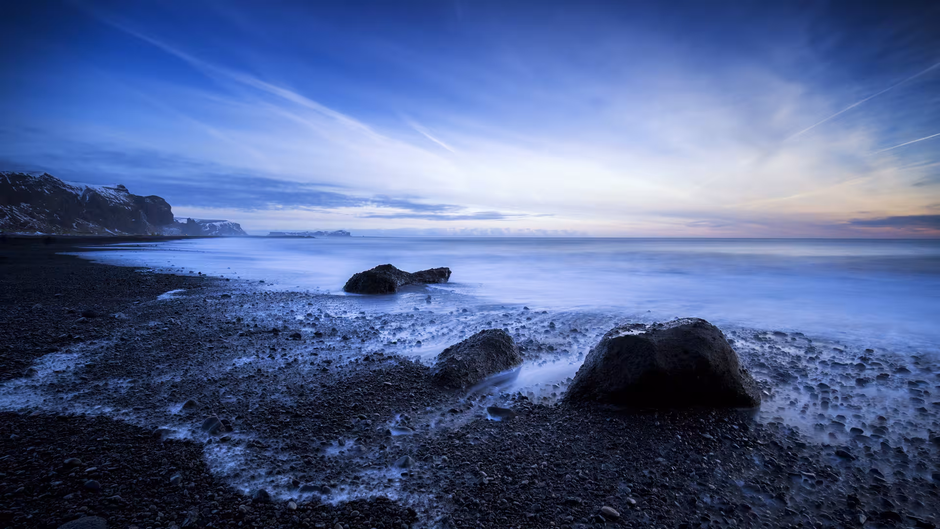 Black pebble beach with dark volcanic rocks and silky blue ocean waves at dusk, Iceland south coast