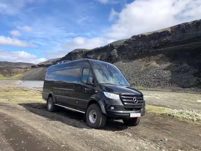 Black Mercedes Sprinter 4x4 minibus parked on Iceland's rugged south coast terrain with volcanic mountains